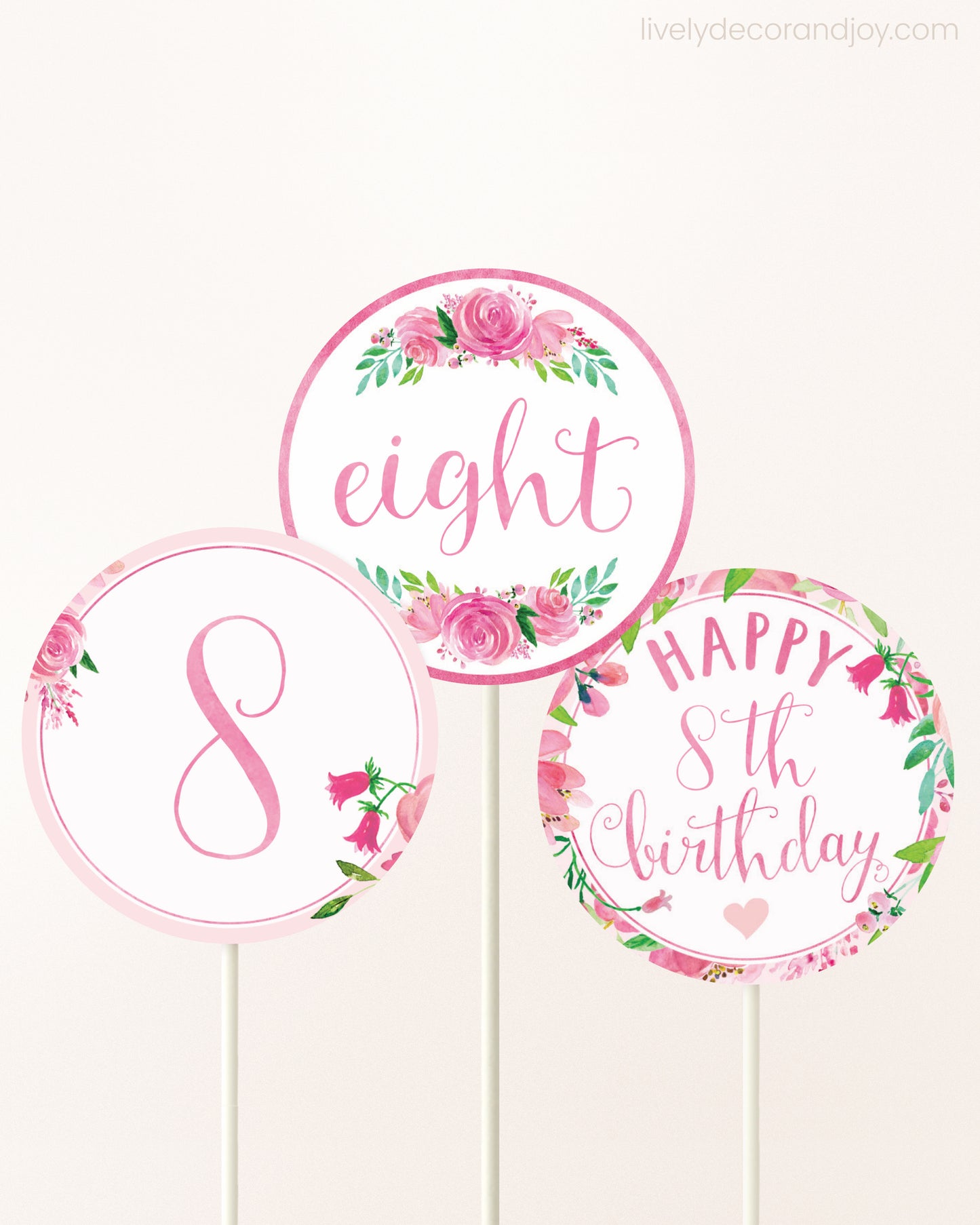 Three cupcakes toppers attached to lollipop sticks. They feature pink watercolor floral designs and pink and gold handwritten text.