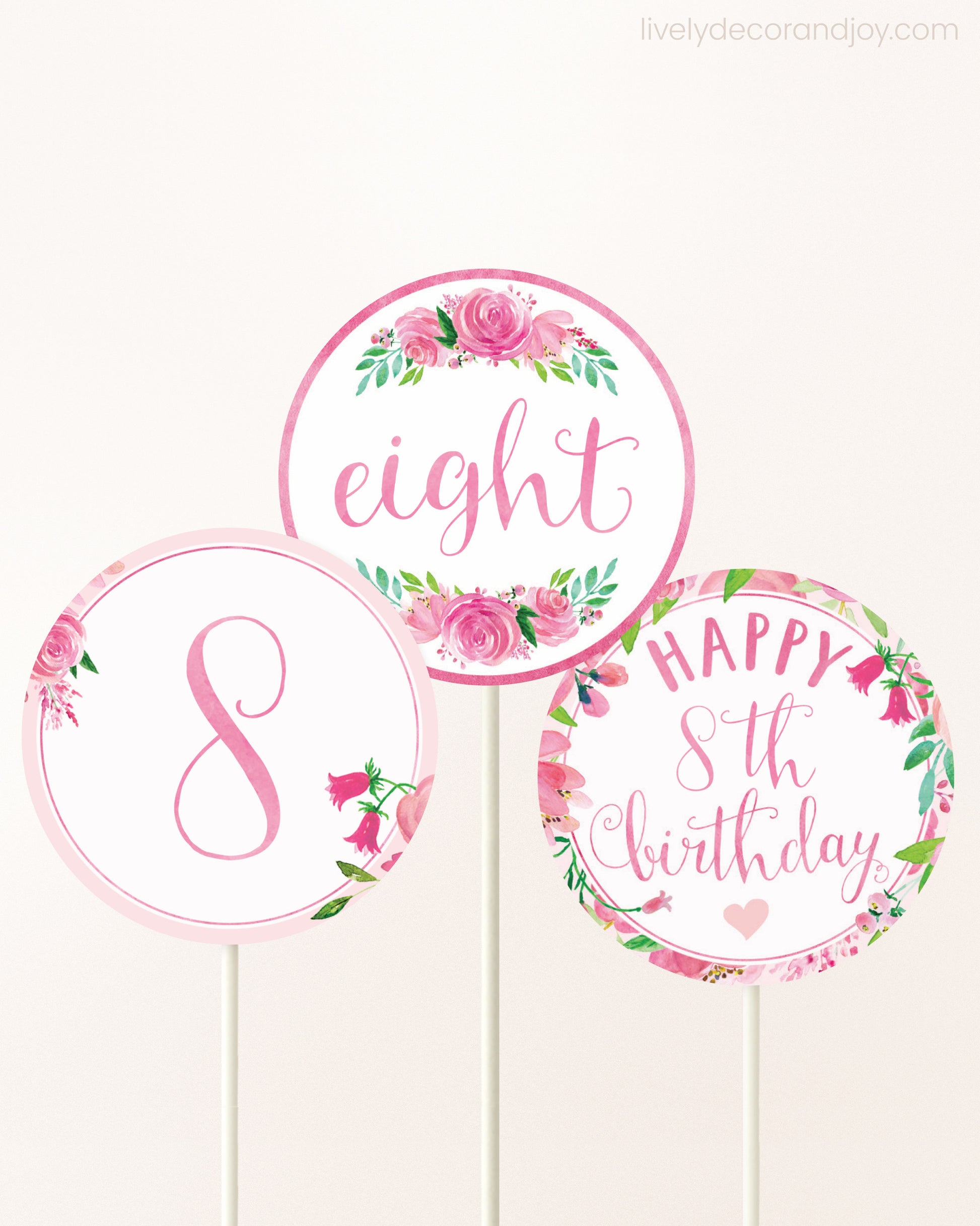 Three cupcakes toppers attached to lollipop sticks. They feature pink watercolor floral designs and pink and gold handwritten text.