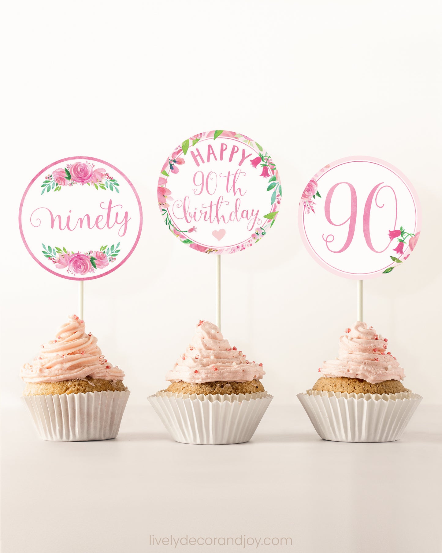 Three cupcakes side by side. Each has a round cupcake topper with pink watercolor flowers and pink and gold letters.