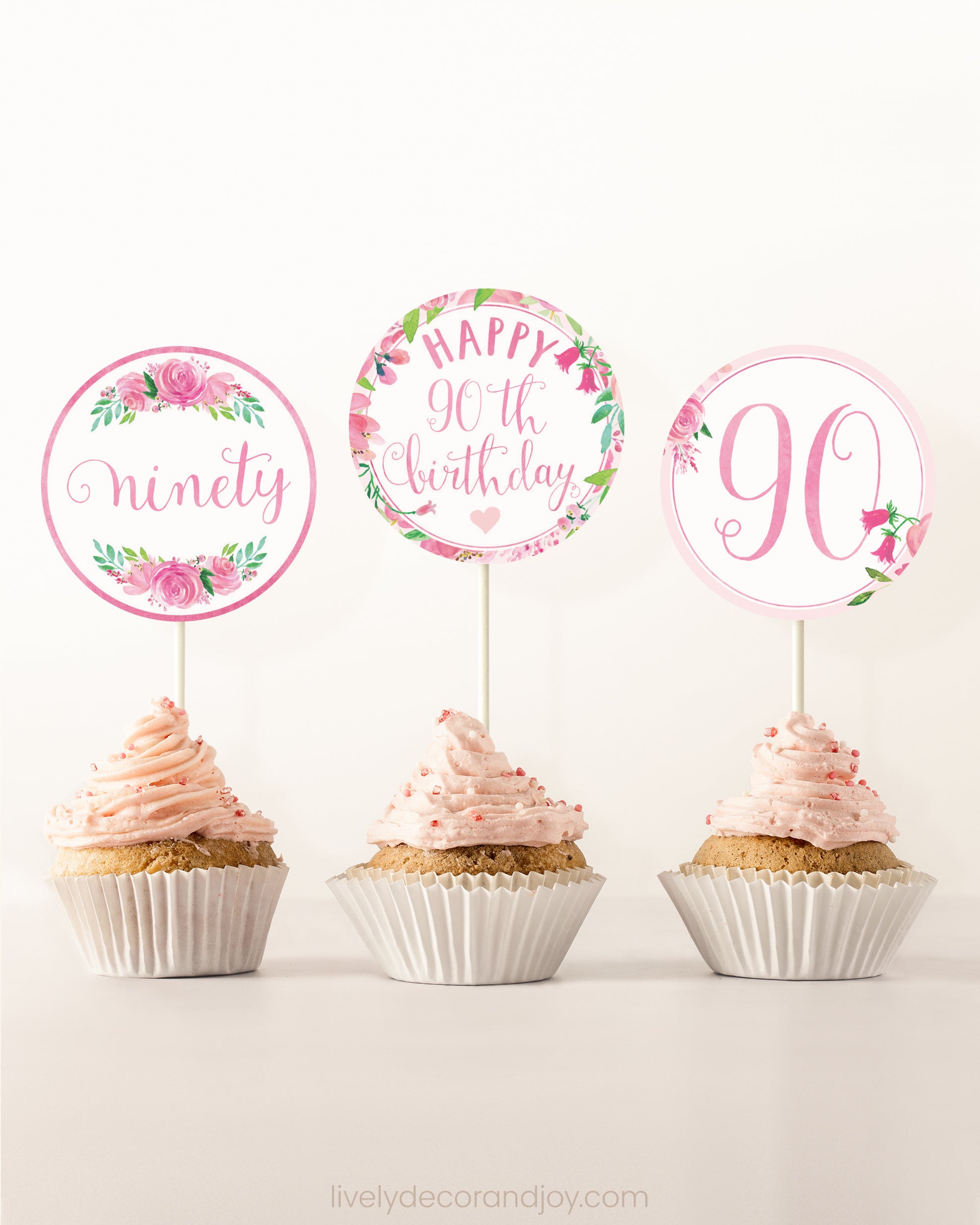 Three cupcakes side by side. Each has a round cupcake topper with pink watercolor flowers and pink and gold letters.