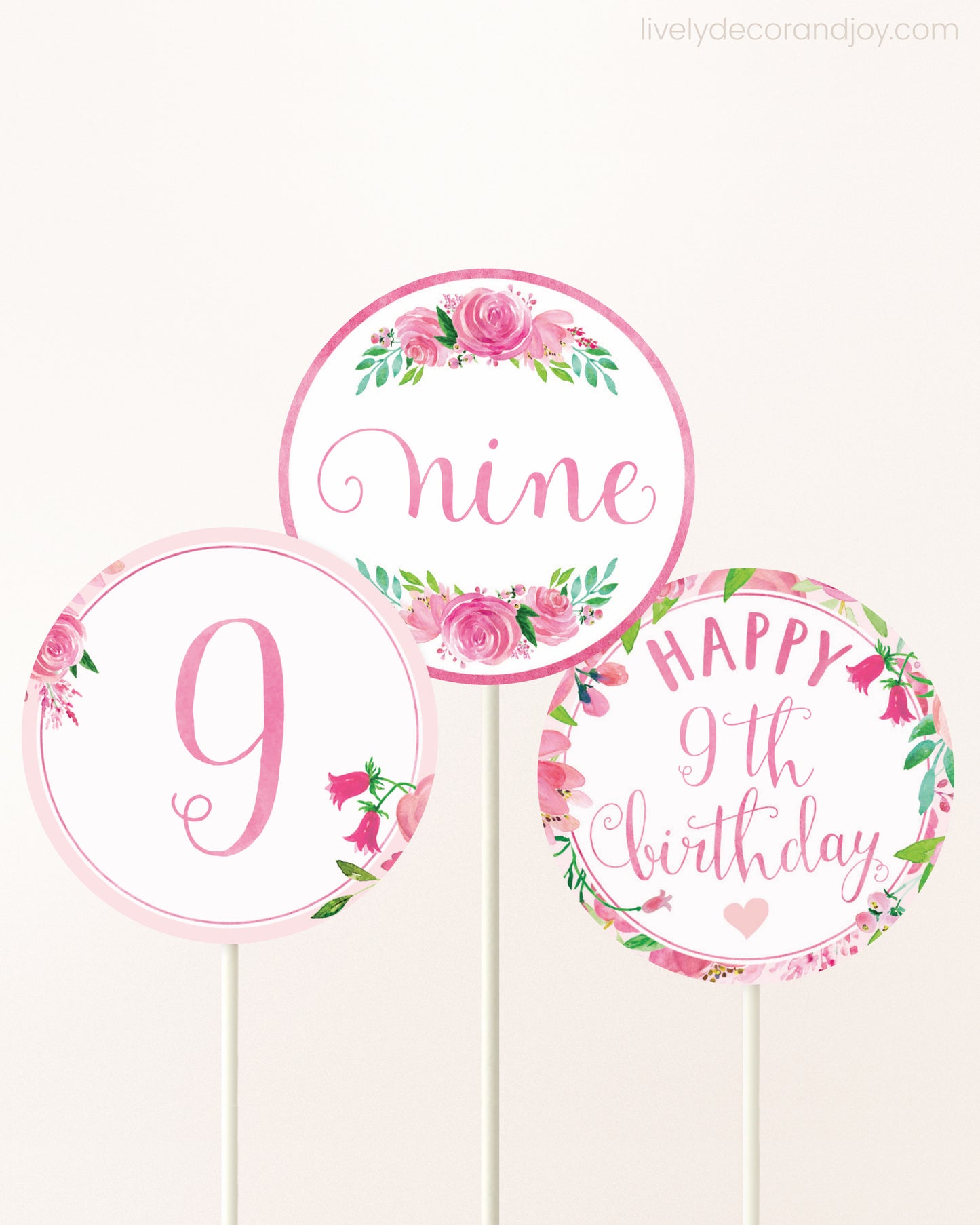 Three DIY toppers attached to lollipop sticks. They show printable cupcake topper designs with pink watercolor flowers.