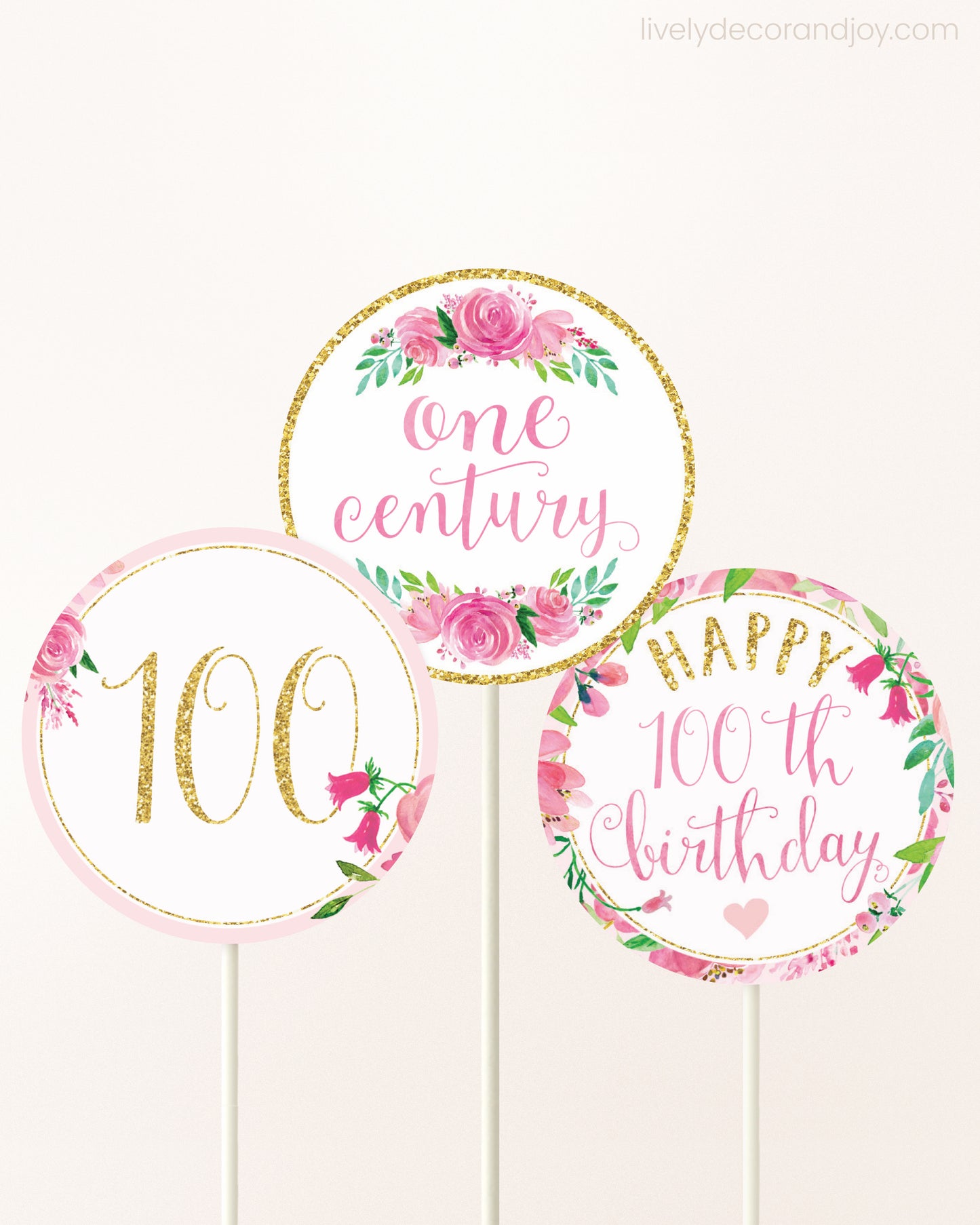 Three cupcakes toppers attached to lollipop sticks. They feature pink watercolor floral designs and pink and gold handwritten text.