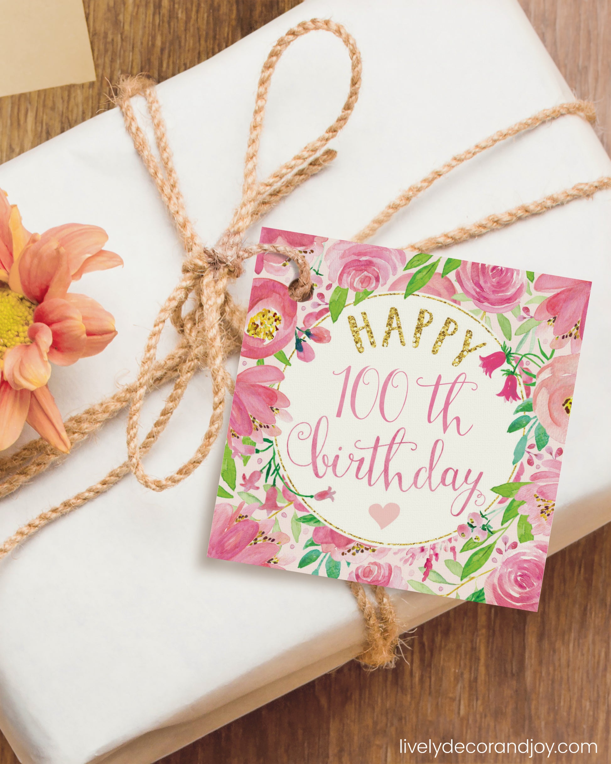 A square gift tag is attached to a birthday gift on a wooden table.