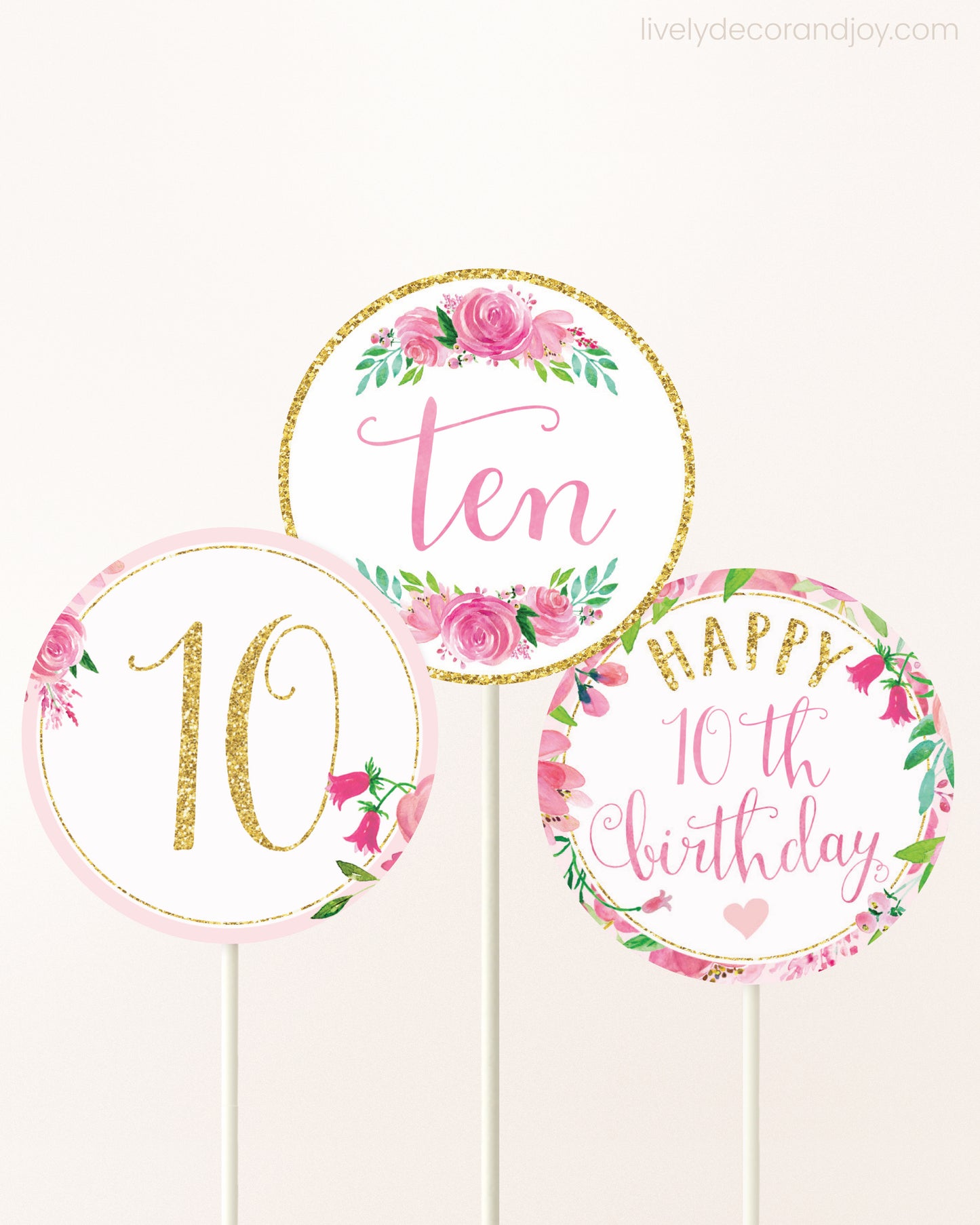 Three cupcakes toppers attached to lollipop sticks. They feature pink watercolor floral designs and pink and gold handwritten text.