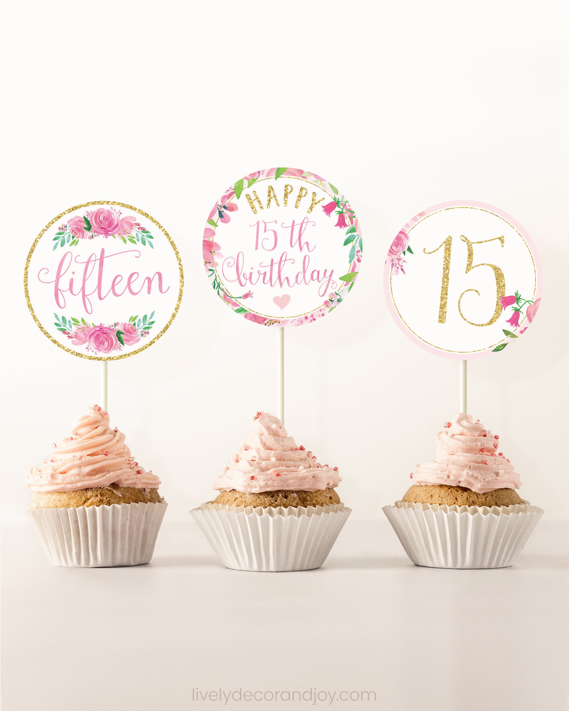 Three cupcakes on a dessert table. Each has a round cupcake topper with pink watercolor floral designs and pink and gold letters.