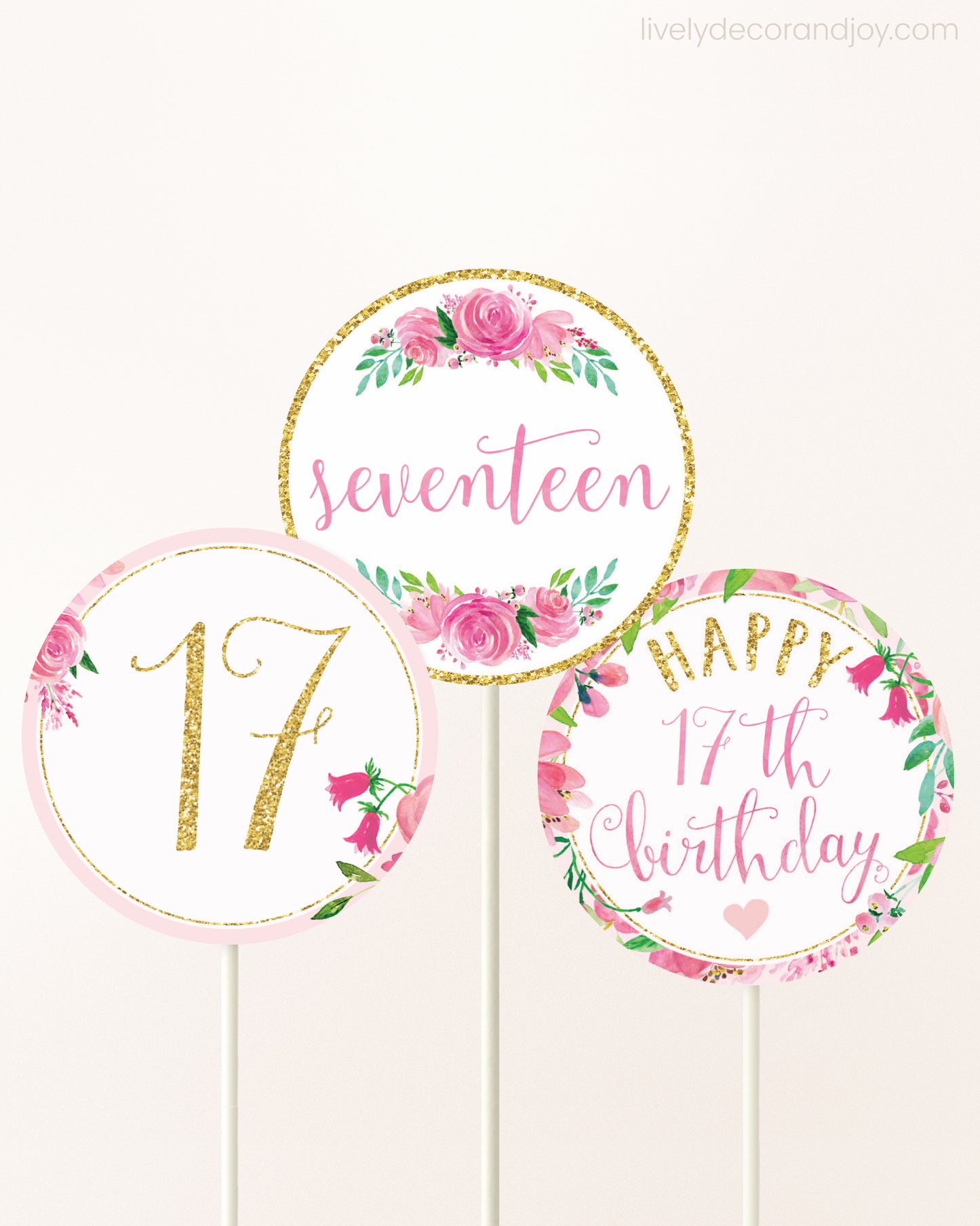 Three cupcakes toppers attached to lollipop sticks. They feature pink watercolor floral designs and pink and gold handwritten text.