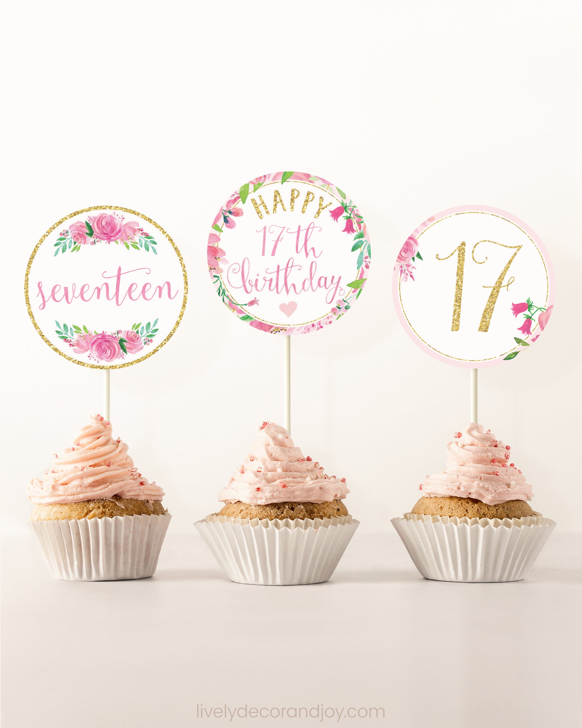 Three cupcakes on a dessert table. Each has a round cupcake topper with pink watercolor floral designs and pink and gold letters.