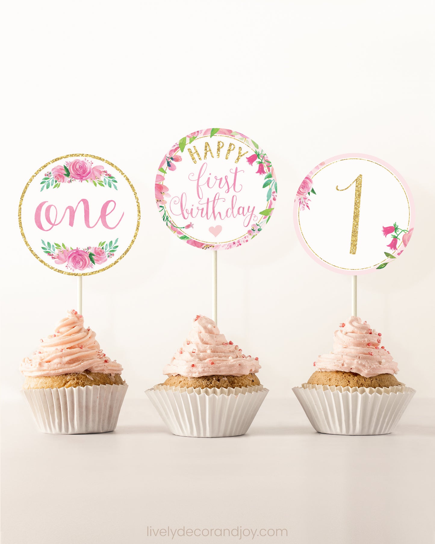 Three cupcakes side by side. Each has a round cupcake topper with pink watercolor flowers and pink and gold letters.