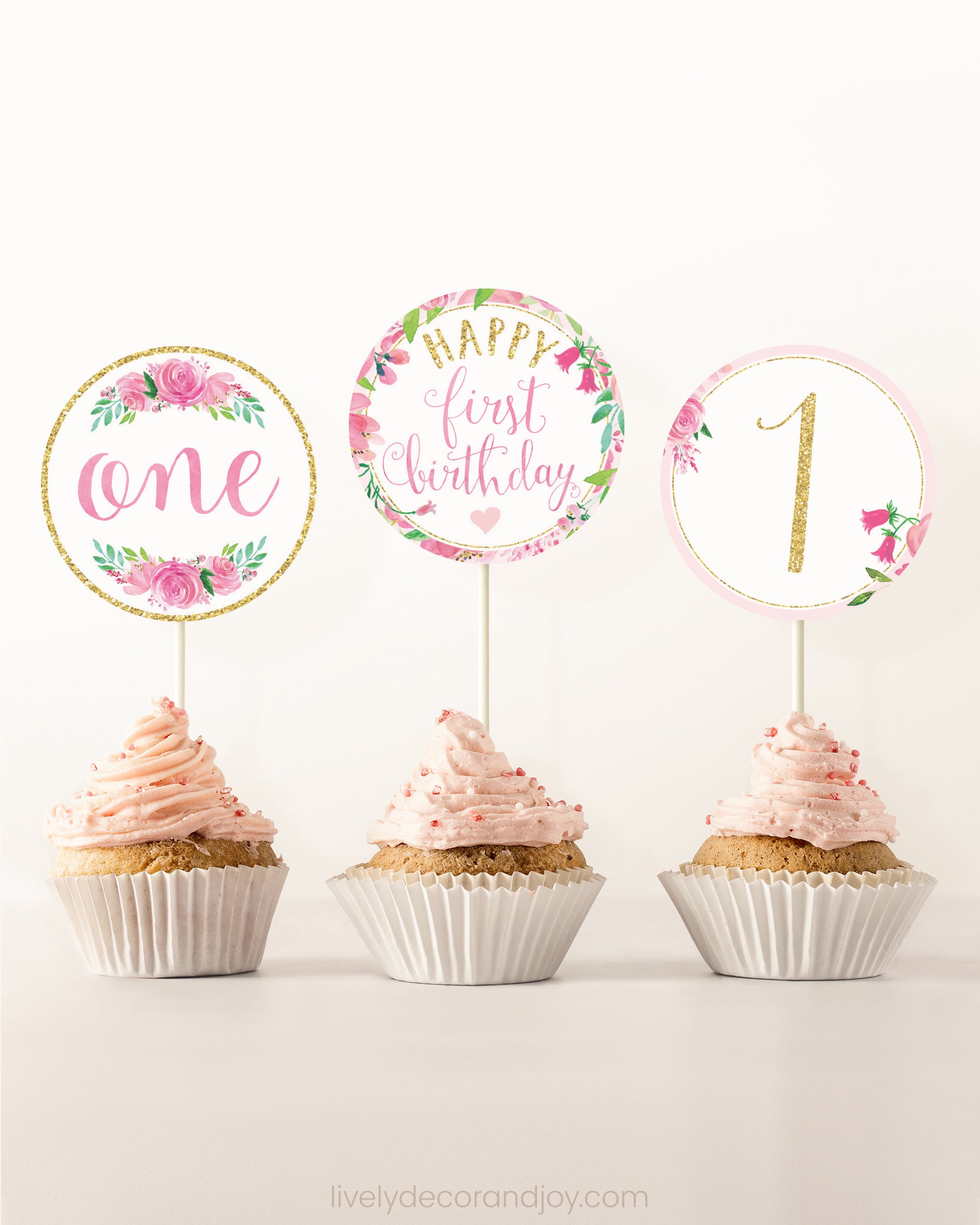 Three cupcakes side by side. Each has a round cupcake topper with pink watercolor flowers and pink and gold letters.