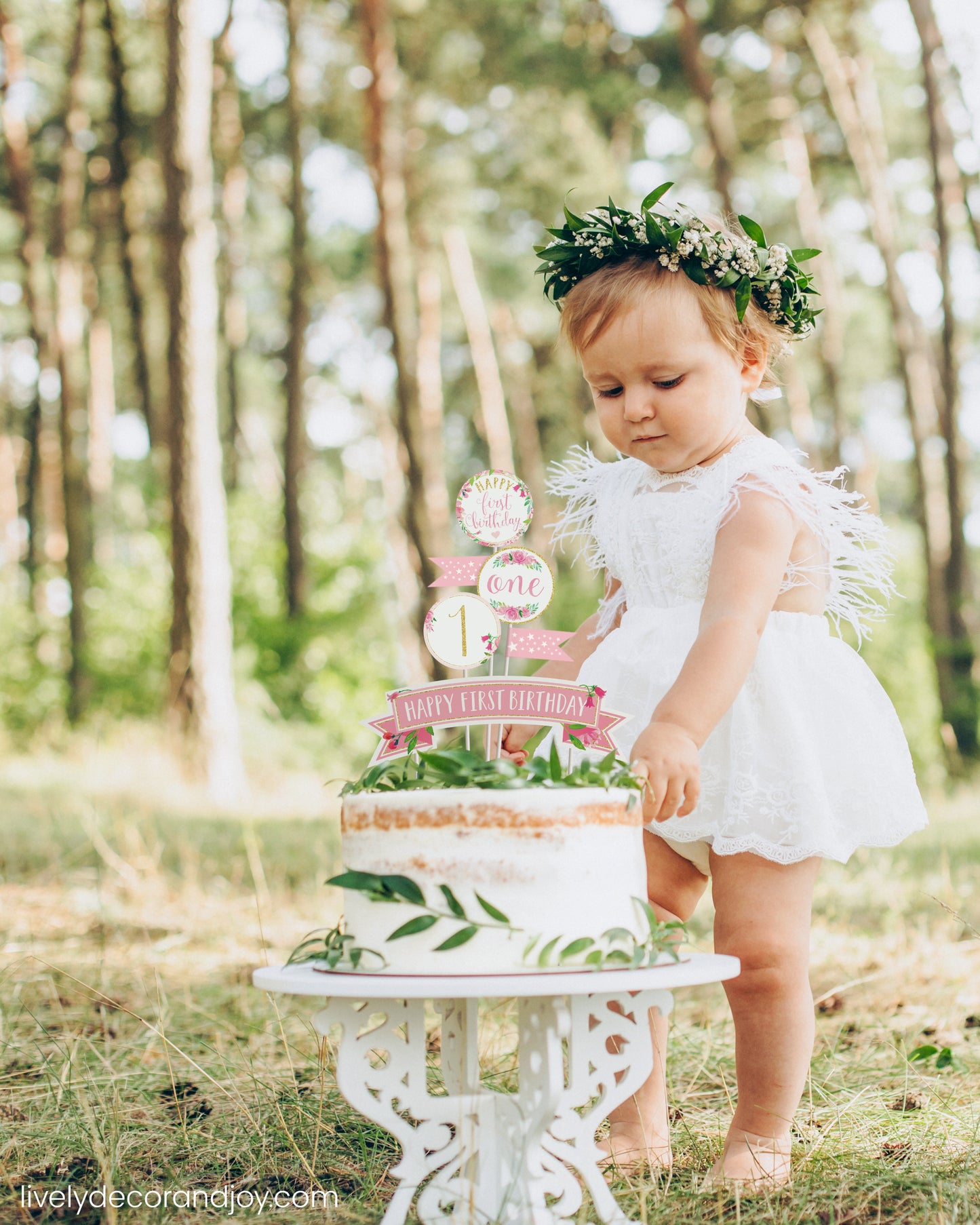 A cute little girl next to her healthy smash cake in a park. It is a rustic sponge cake with a printed cake topper.