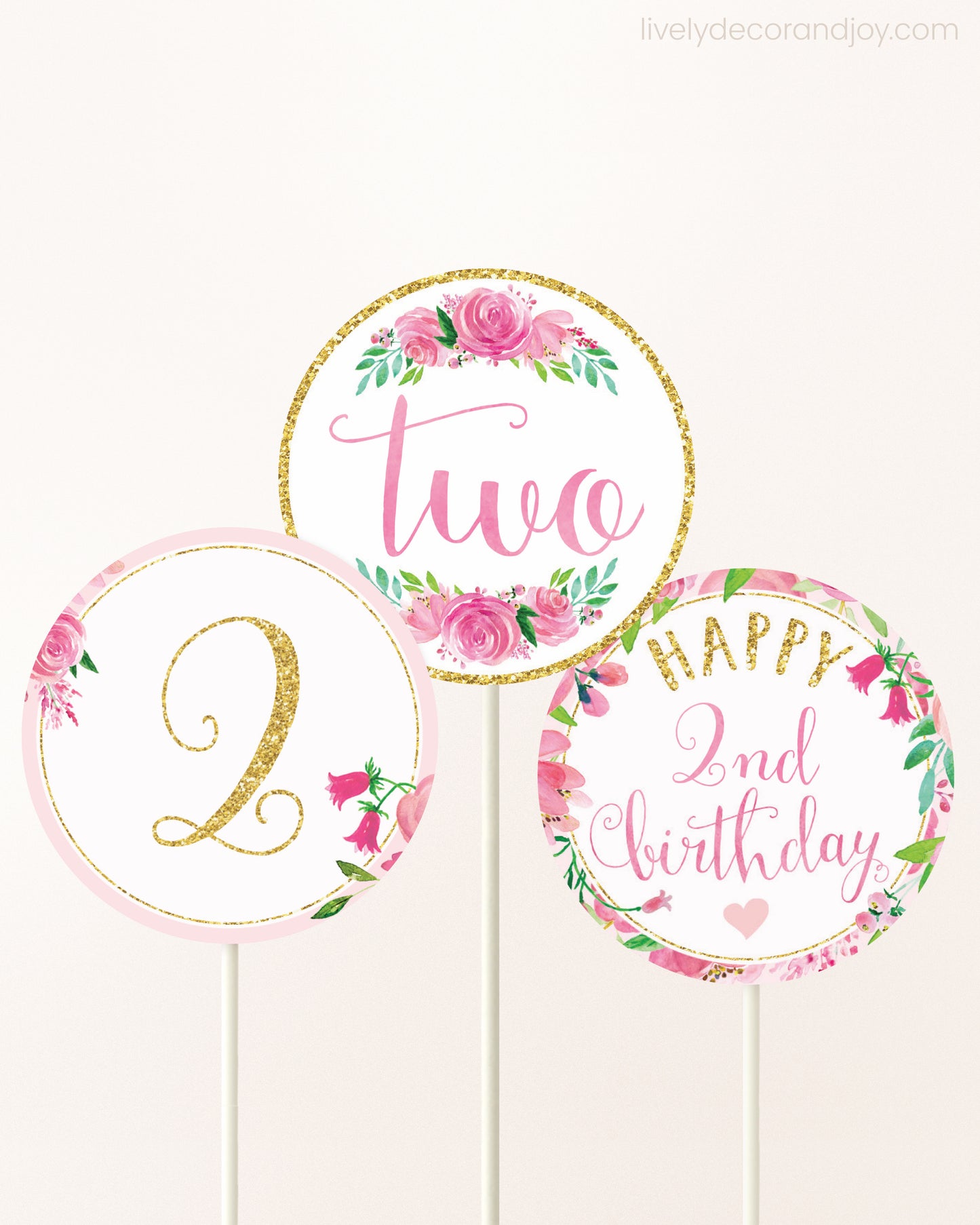 Three cupcakes toppers attached to lollipop sticks. They feature pink watercolor floral designs and pink and gold handwritten text.