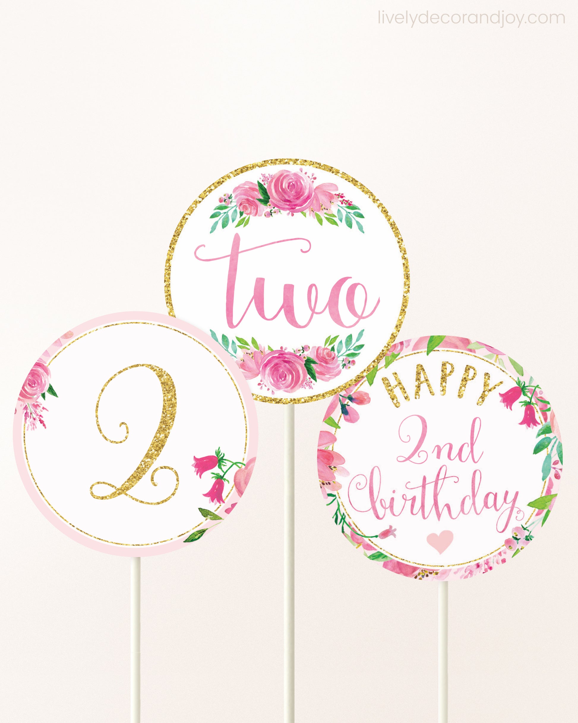 Three cupcakes toppers attached to lollipop sticks. They feature pink watercolor floral designs and pink and gold handwritten text.