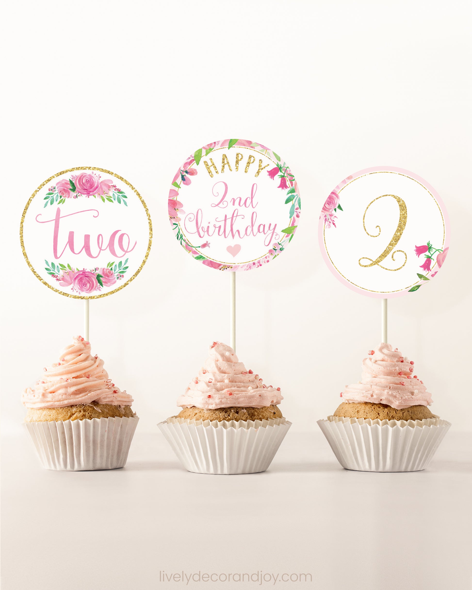 Three cupcakes on a dessert table. Each has a round cupcake topper with pink watercolor floral designs and pink and gold letters.