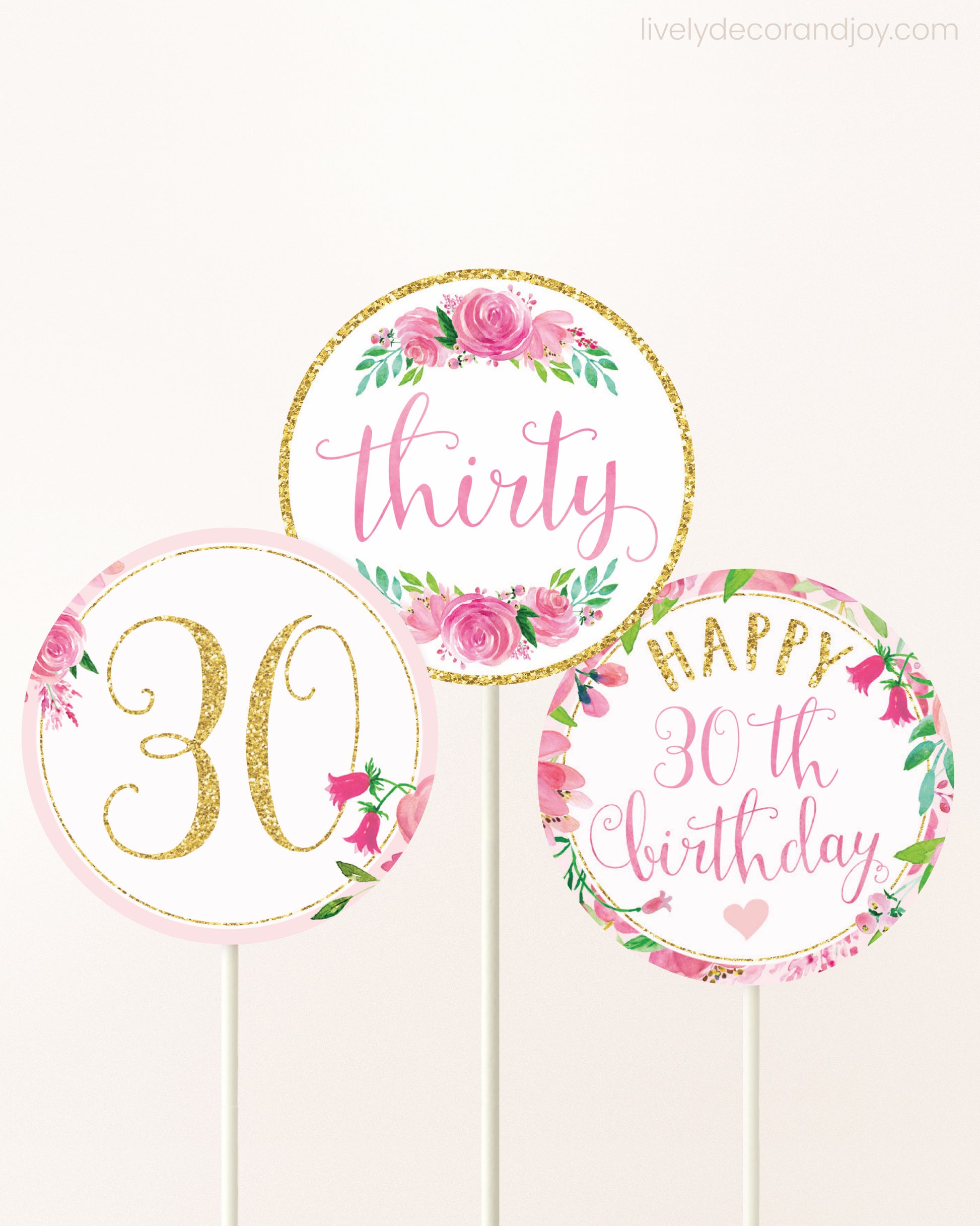 Three cupcakes toppers attached to lollipop sticks. They feature pink watercolor floral designs and pink and gold handwritten text.