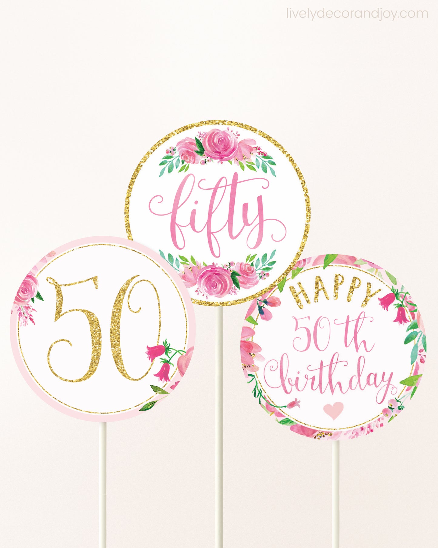 Three DIY toppers attached to lollipop sticks. They show printable cupcake topper designs with pink watercolor flowers.