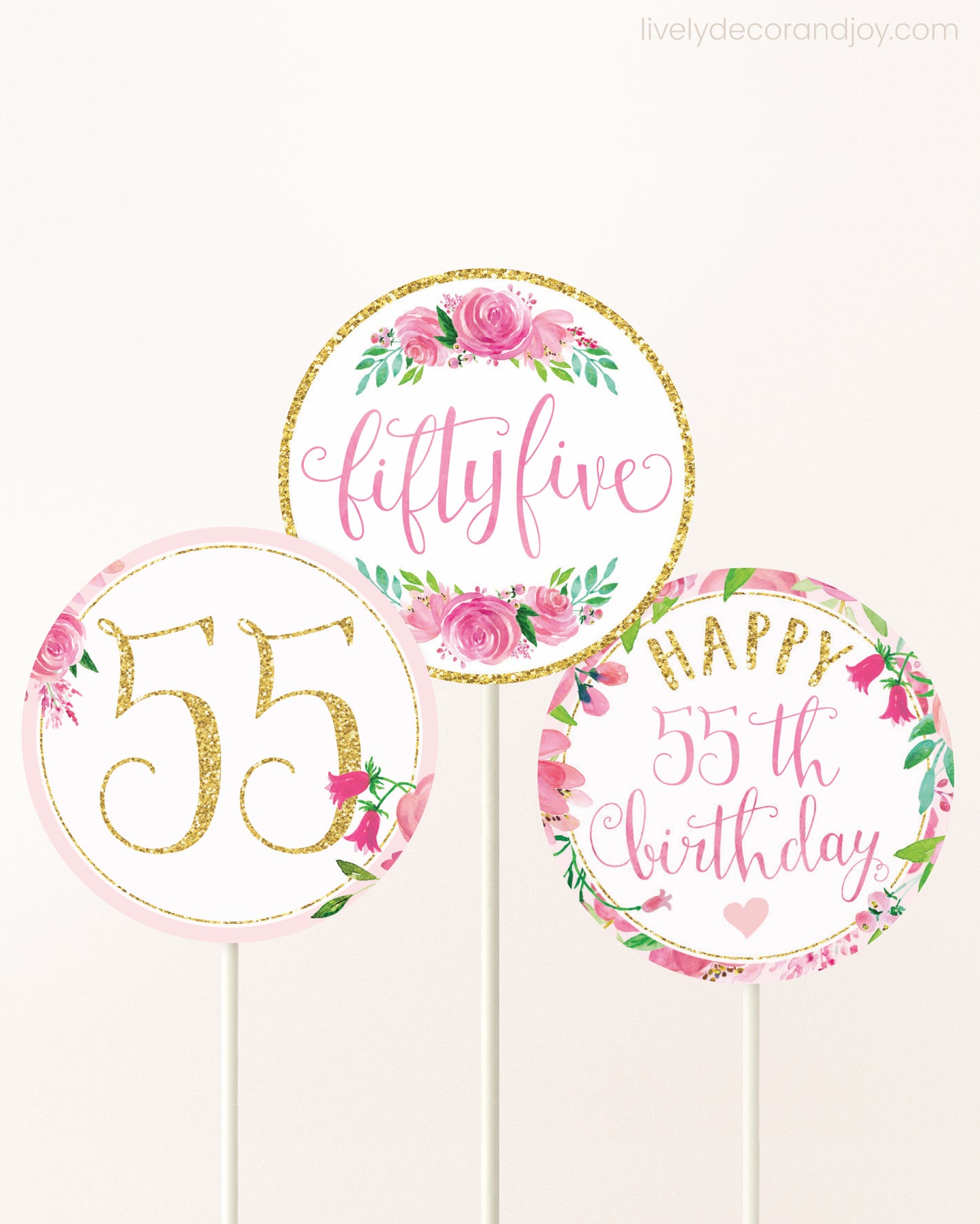 Three cupcakes toppers attached to lollipop sticks. They feature pink watercolor floral designs and pink and gold handwritten text.