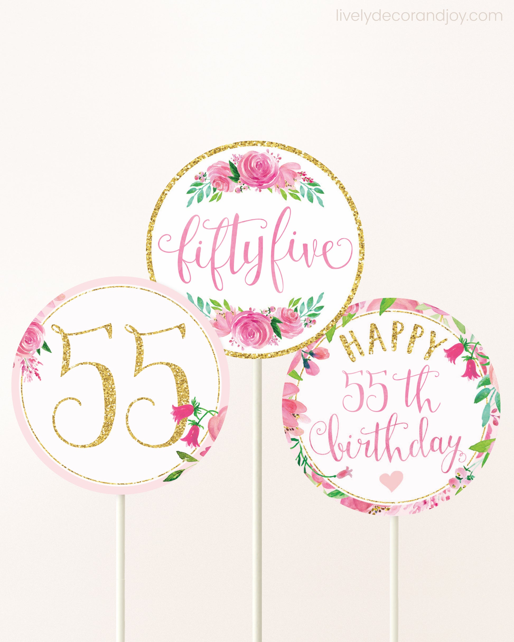 Three cupcakes toppers attached to lollipop sticks. They feature pink watercolor floral designs and pink and gold handwritten text.