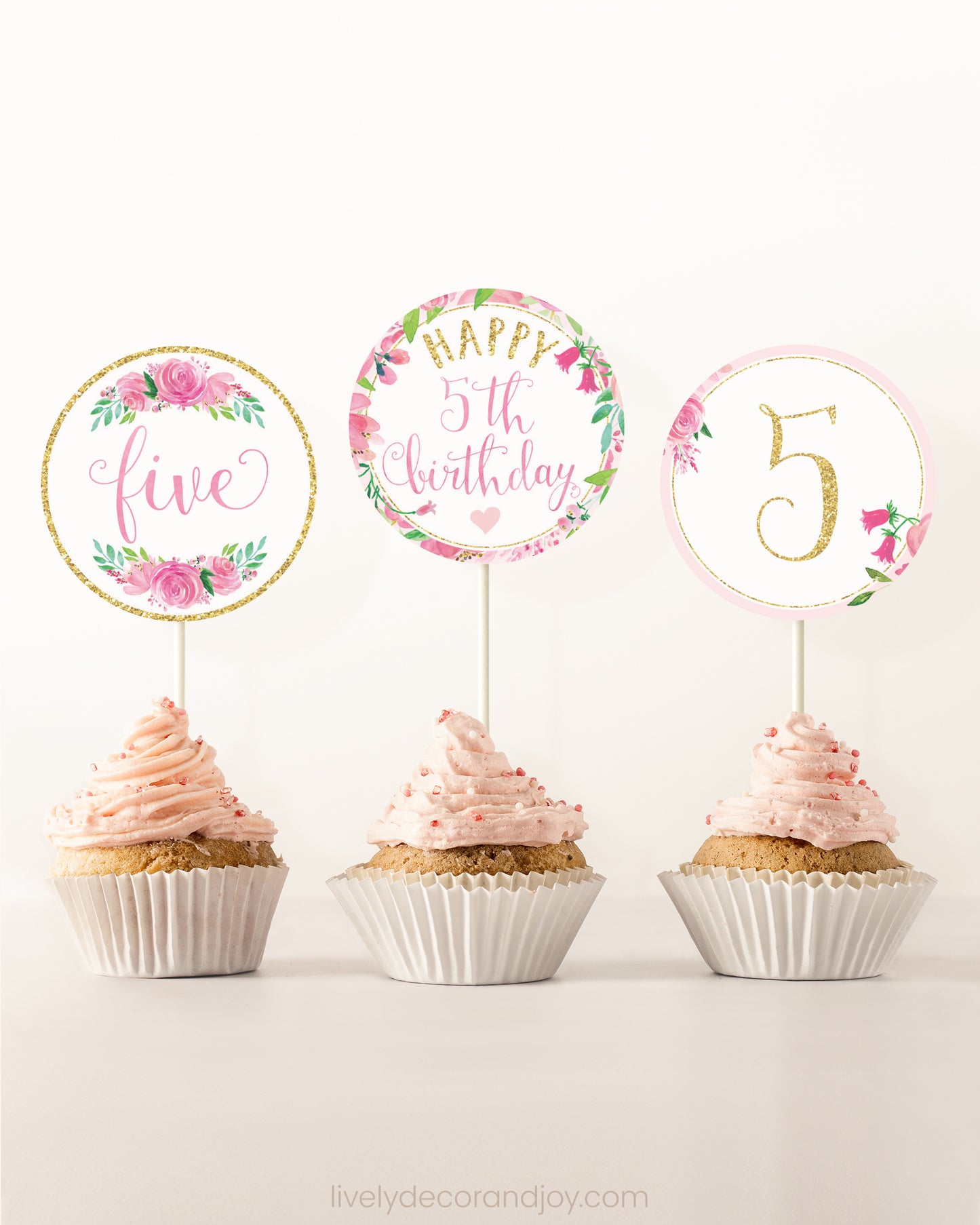 Three cupcakes side by side. Each has a round cupcake topper with pink watercolor flowers and pink and gold letters.