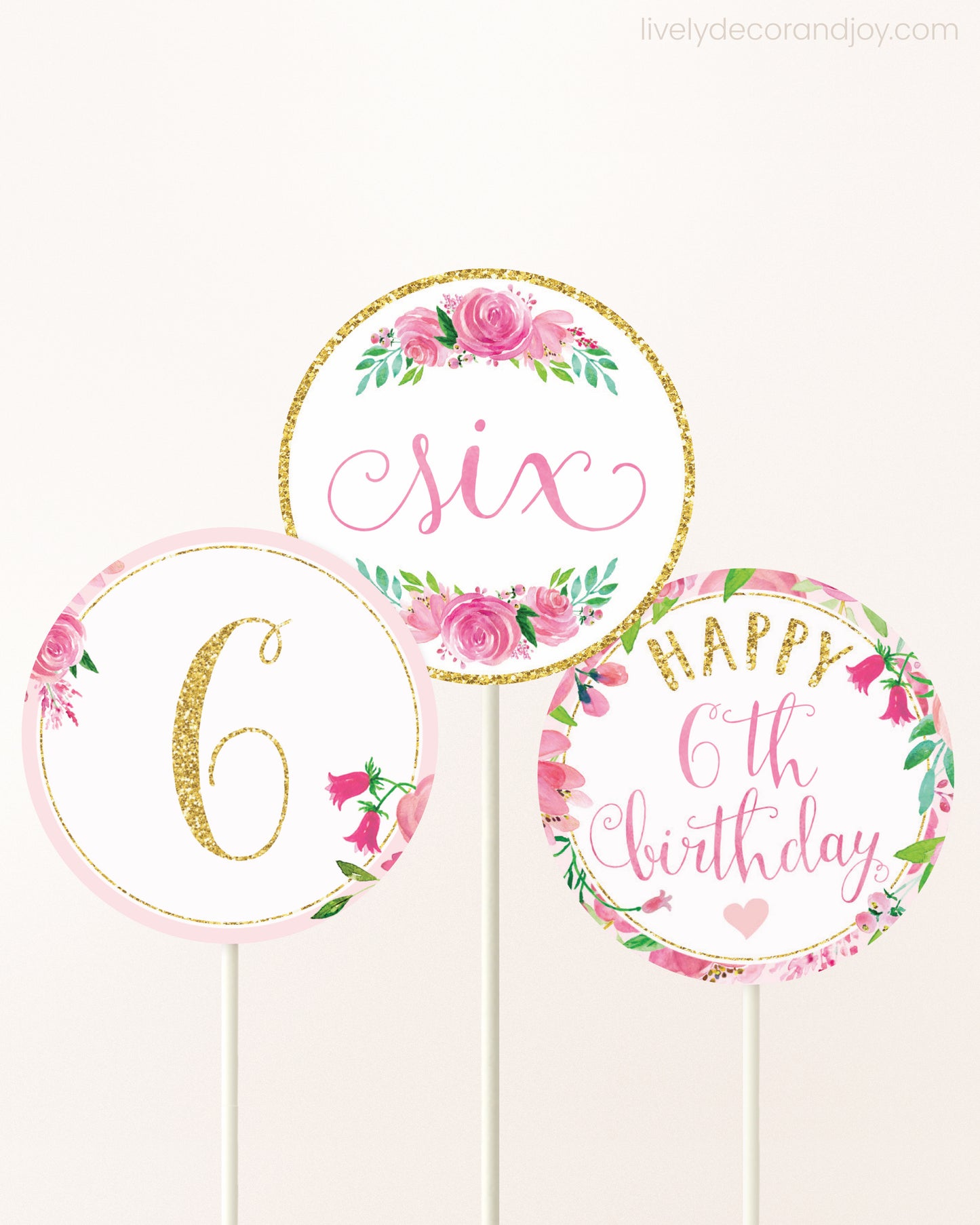 Three cupcakes toppers attached to lollipop sticks. They feature pink watercolor floral designs and pink and gold handwritten text.