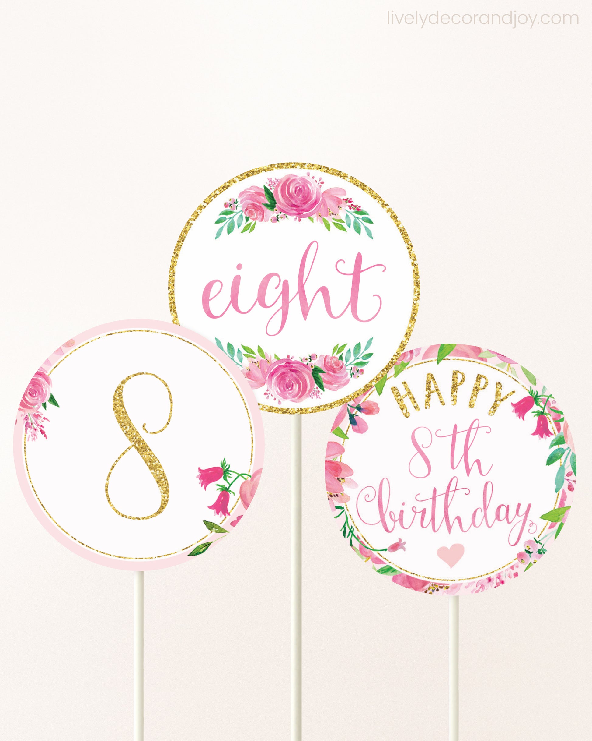 Three cupcakes toppers attached to lollipop sticks. They feature pink watercolor floral designs and pink and gold handwritten text.
