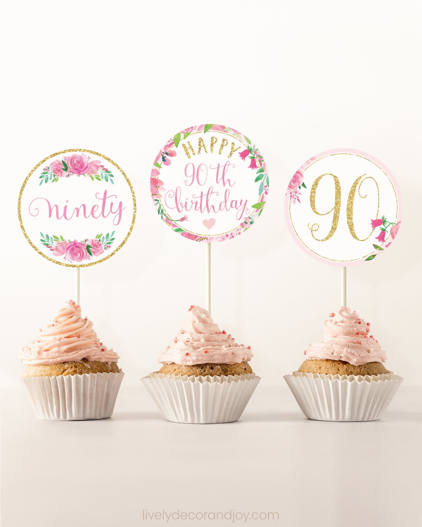 Three cupcakes side by side. Each has a round cupcake topper with pink watercolor flowers and pink and gold letters.