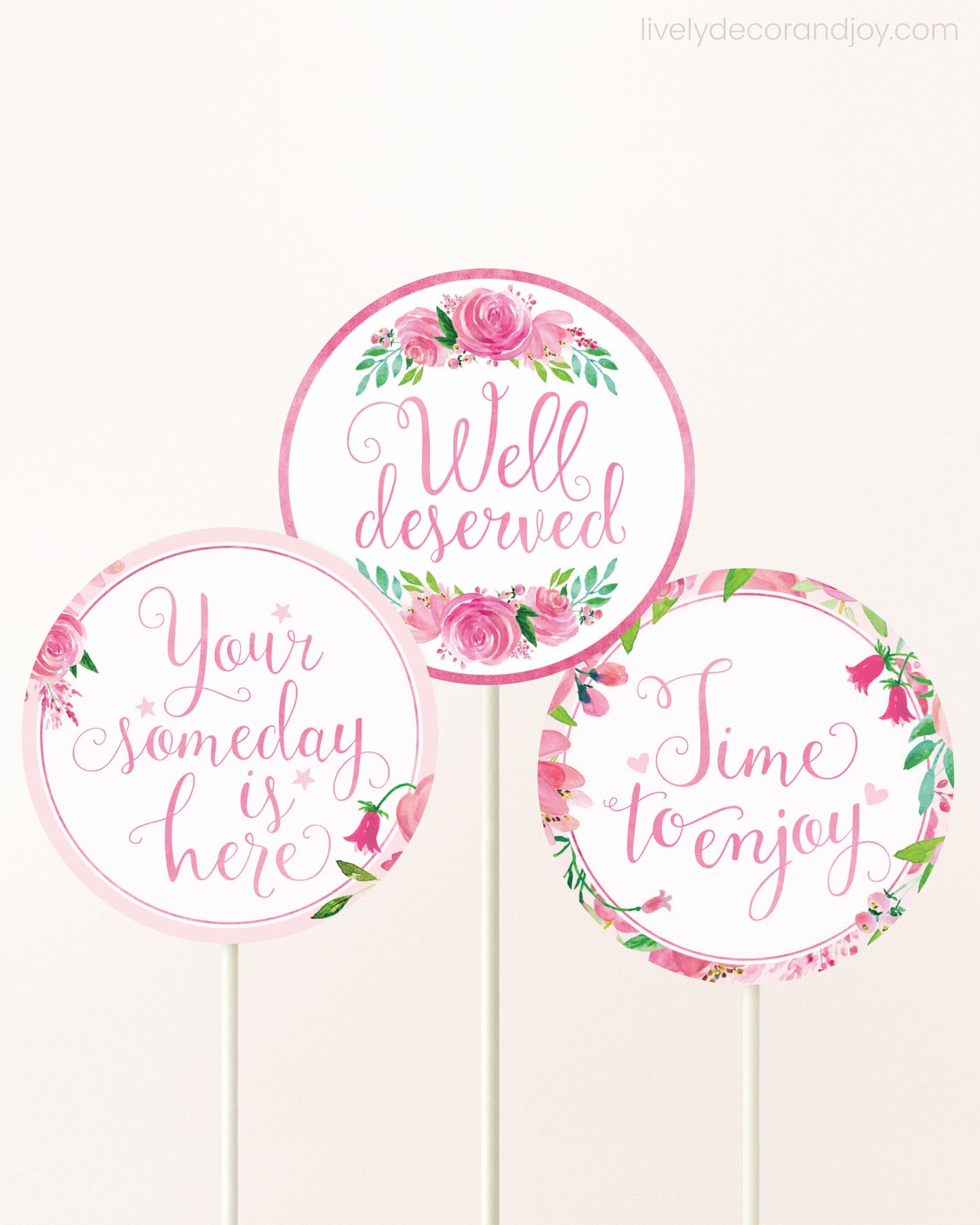 Three DIY toppers attached to lollipop sticks. They show printable cupcake topper designs with pink watercolor flowers.