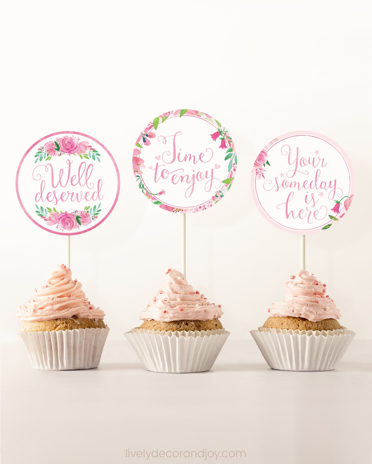 Three cupcakes side by side. Each has a round cupcake topper with pink watercolor flowers and pink and gold letters.