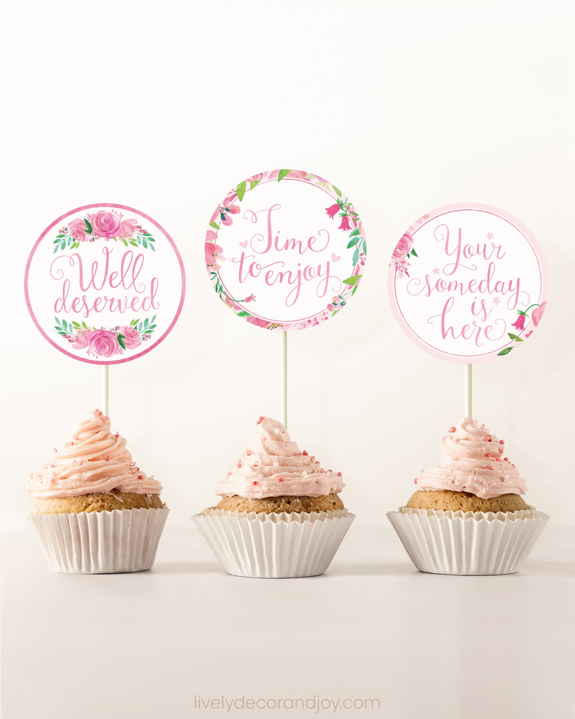Three cupcakes side by side. Each has a round cupcake topper with pink watercolor flowers and pink and gold letters.