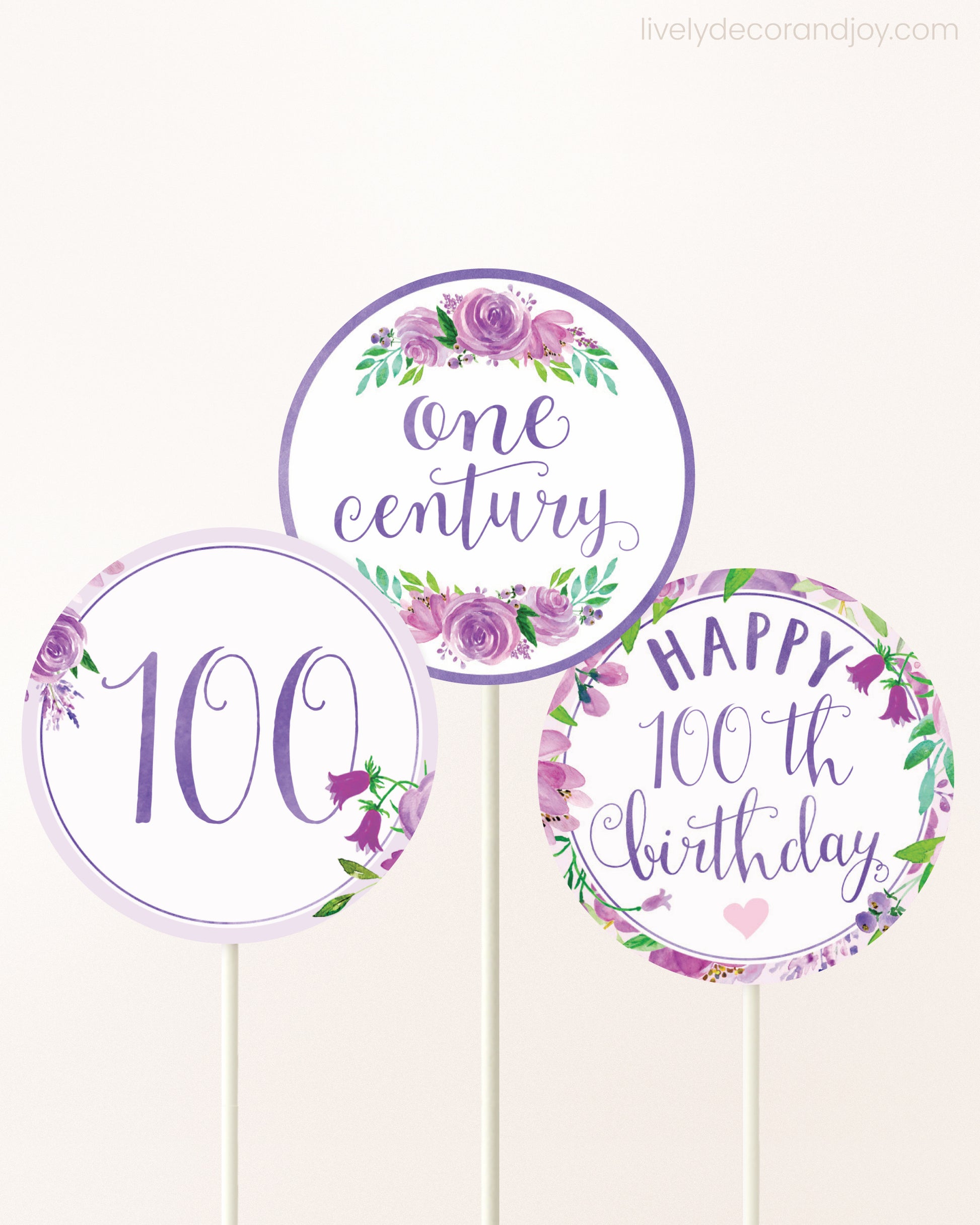 Three cupcakes toppers attached to lollipop sticks. They feature purple watercolor floral designs and purple and gold handwritten text.