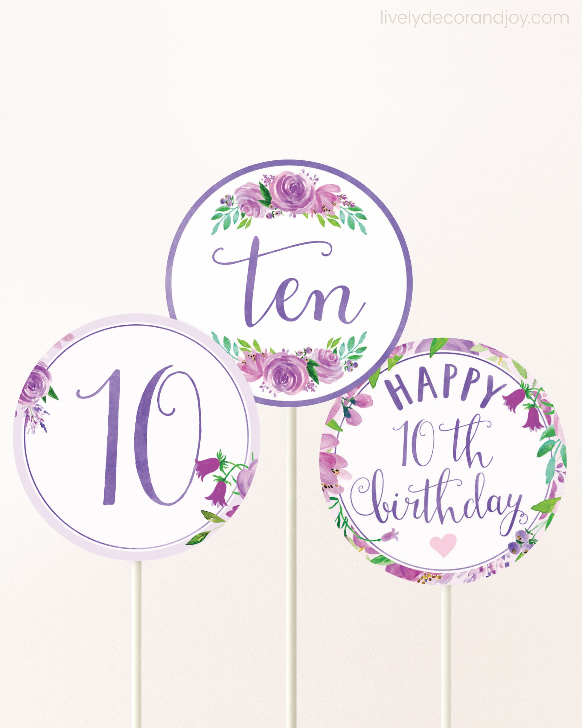 Three cupcakes toppers attached to lollipop sticks. They feature purple watercolor floral designs and purple and gold handwritten text.