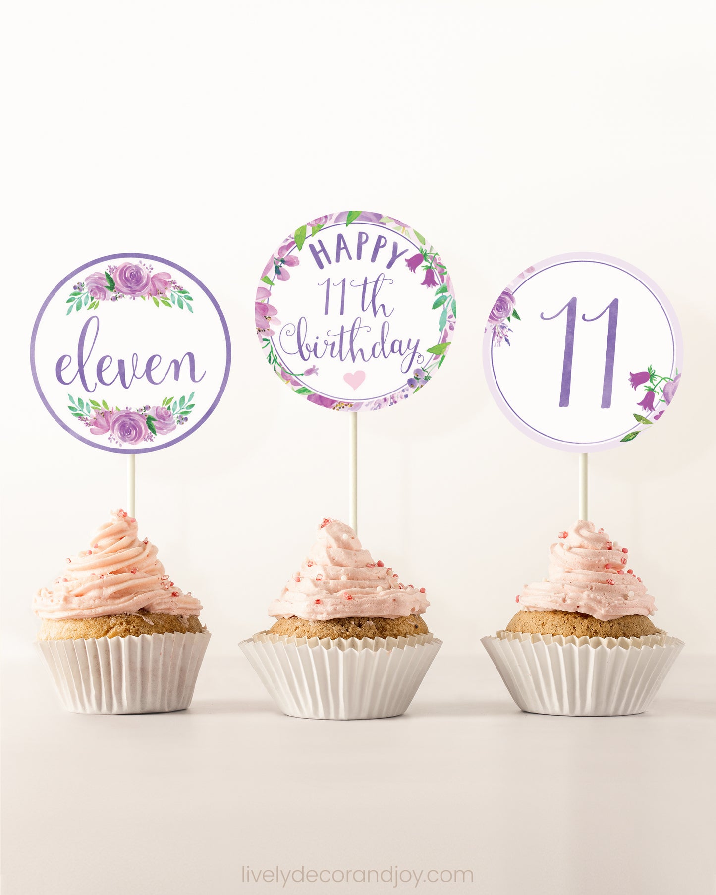 Three cupcakes side by side. Each has a round cupcake topper with purple watercolor flowers and purple and gold letters.