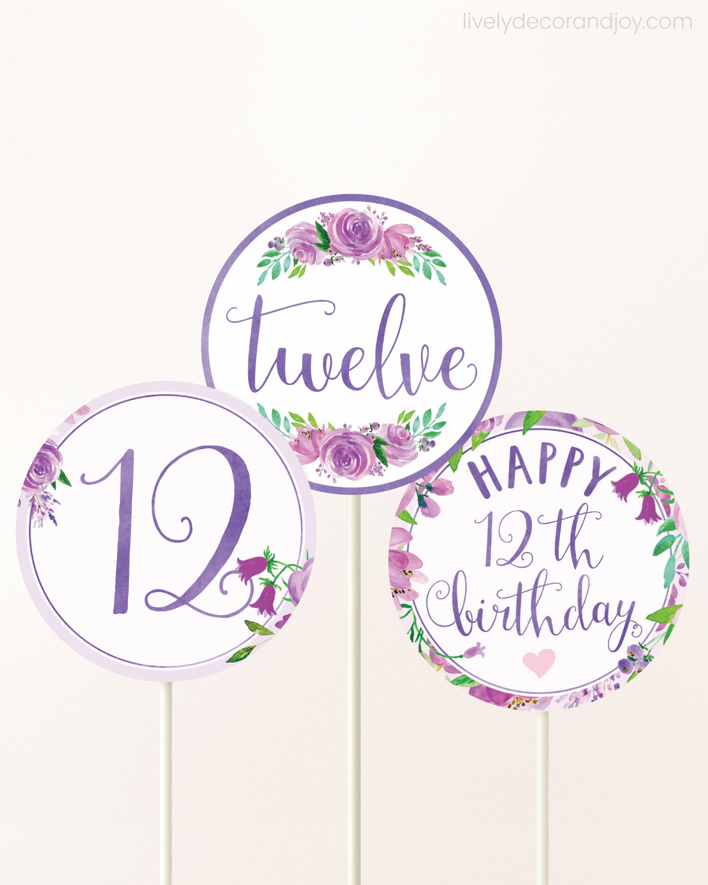 Three cupcakes toppers attached to lollipop sticks. They feature purple watercolor floral designs and purple and gold handwritten text.