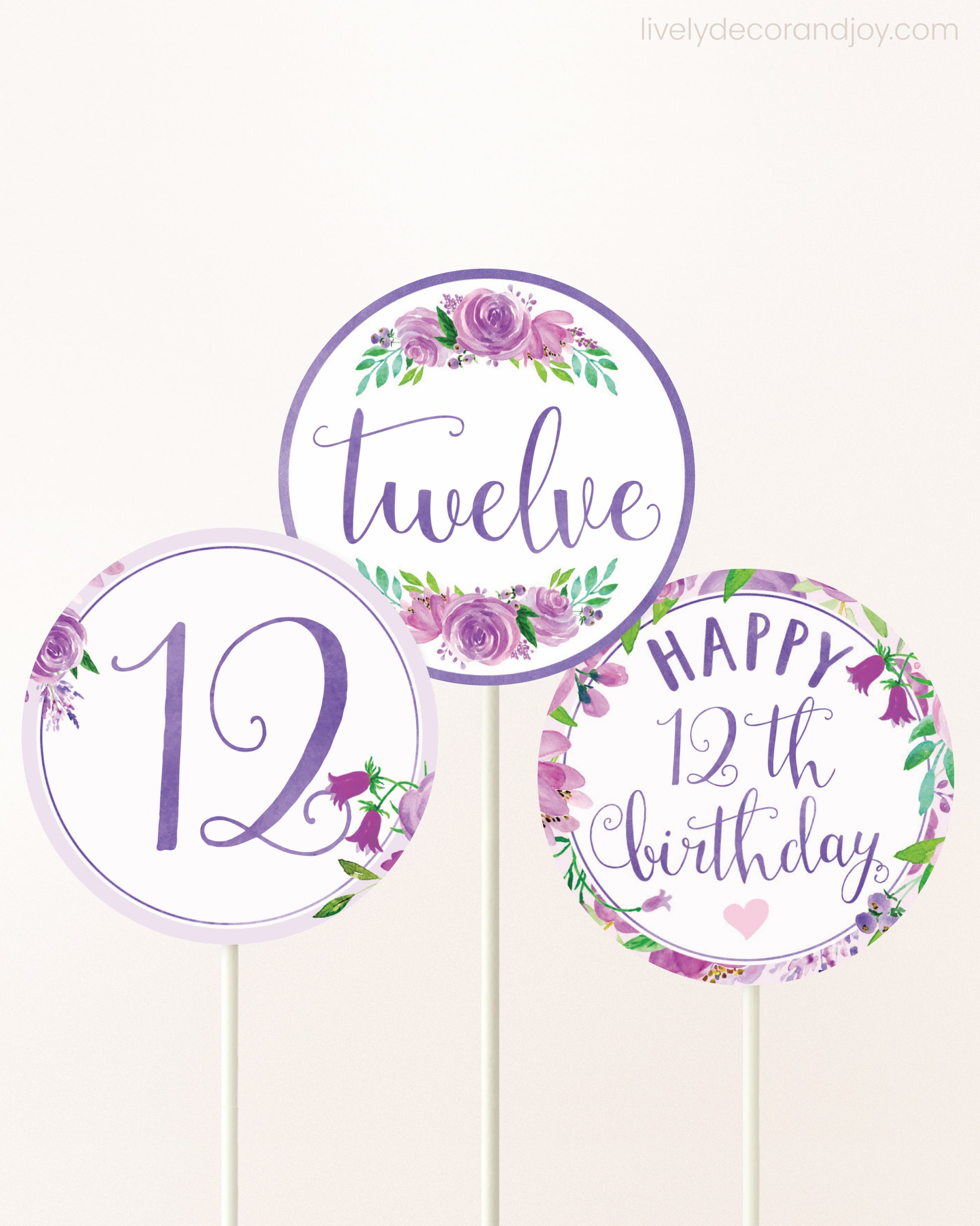 Three cupcakes toppers attached to lollipop sticks. They feature purple watercolor floral designs and purple and gold handwritten text.