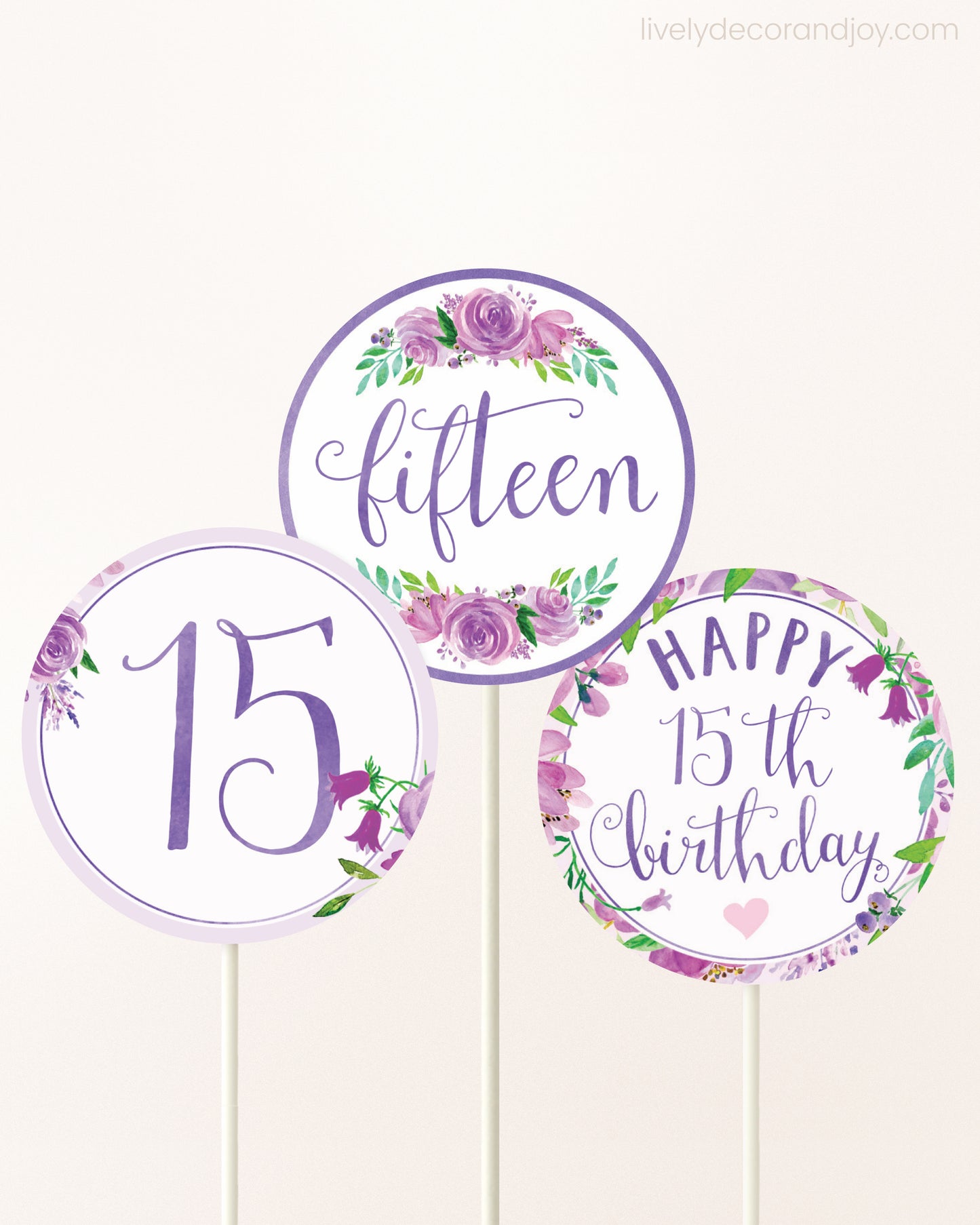 Three cupcakes toppers attached to lollipop sticks. They feature purple watercolor floral designs and purple and gold handwritten text.
