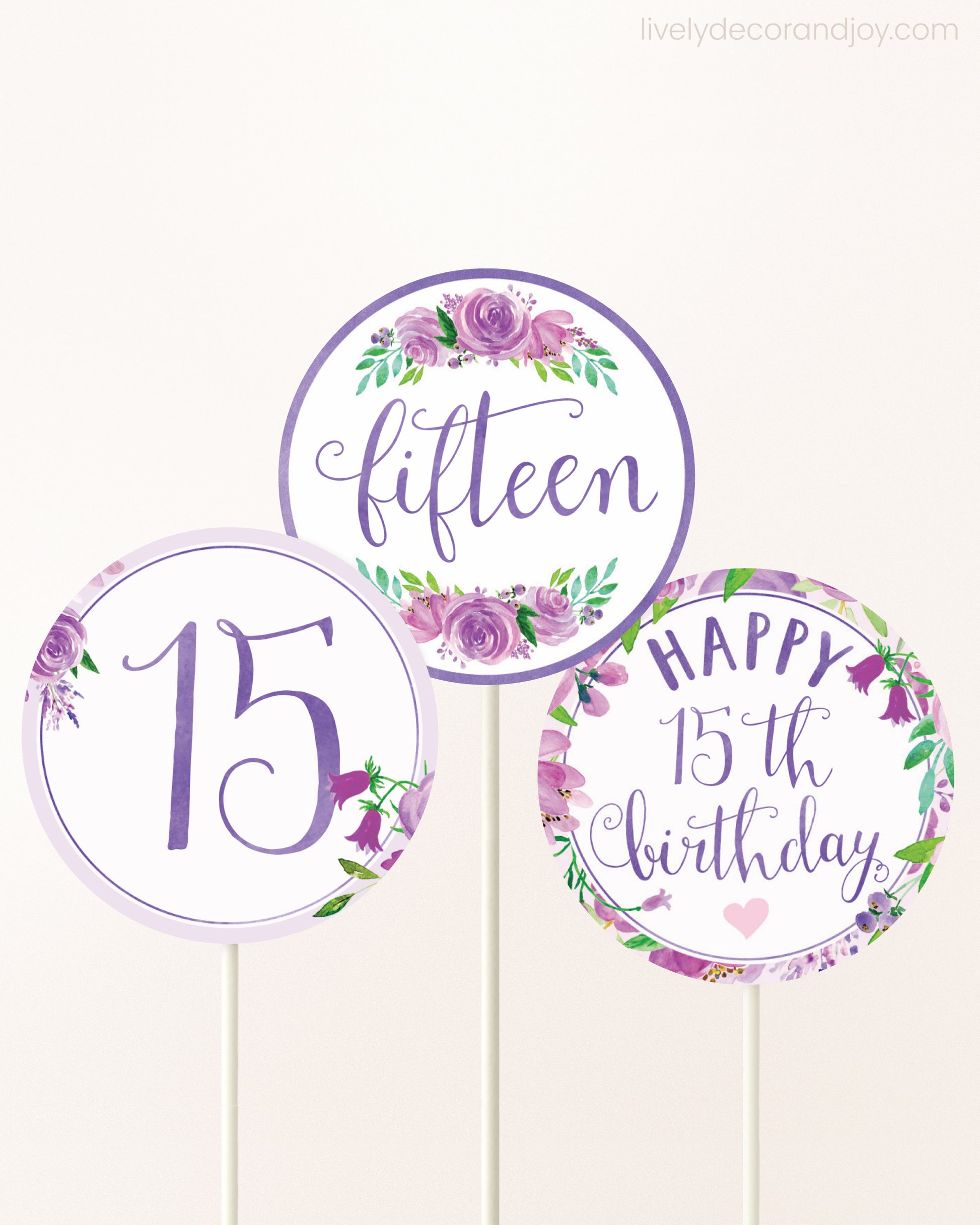 Three cupcakes toppers attached to lollipop sticks. They feature purple watercolor floral designs and purple and gold handwritten text.