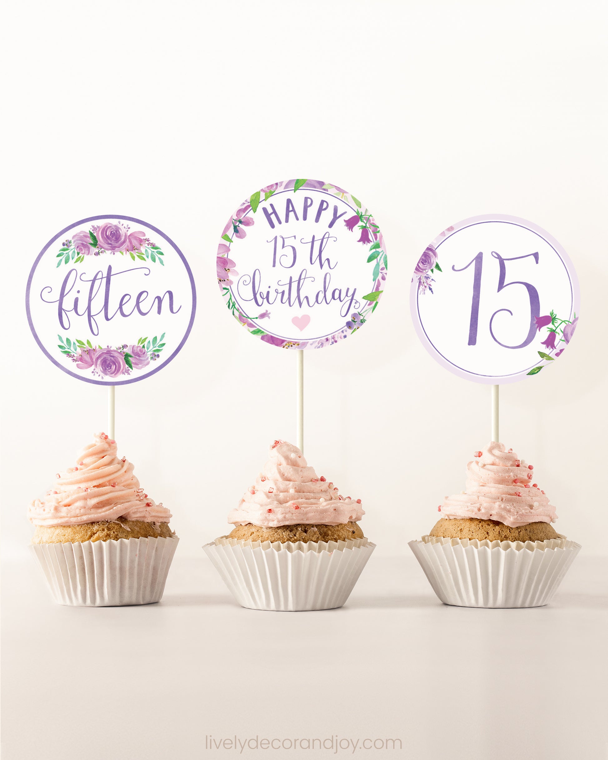 Three cupcakes on a dessert table. Each has a round cupcake topper with purple watercolor floral designs and purple and gold letters.