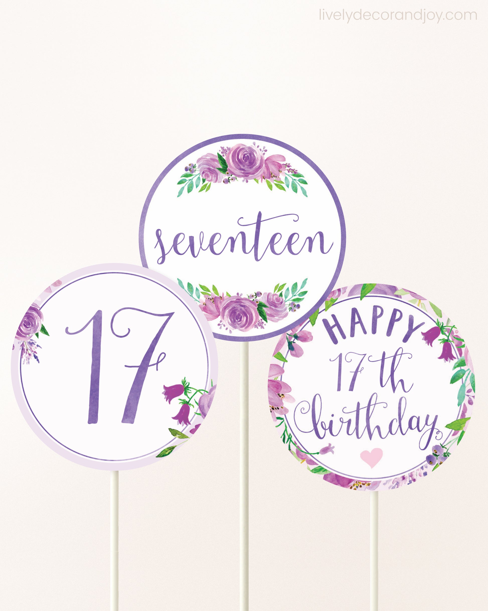 Three cupcakes toppers attached to lollipop sticks. They feature purple watercolor floral designs and purple and gold handwritten text.