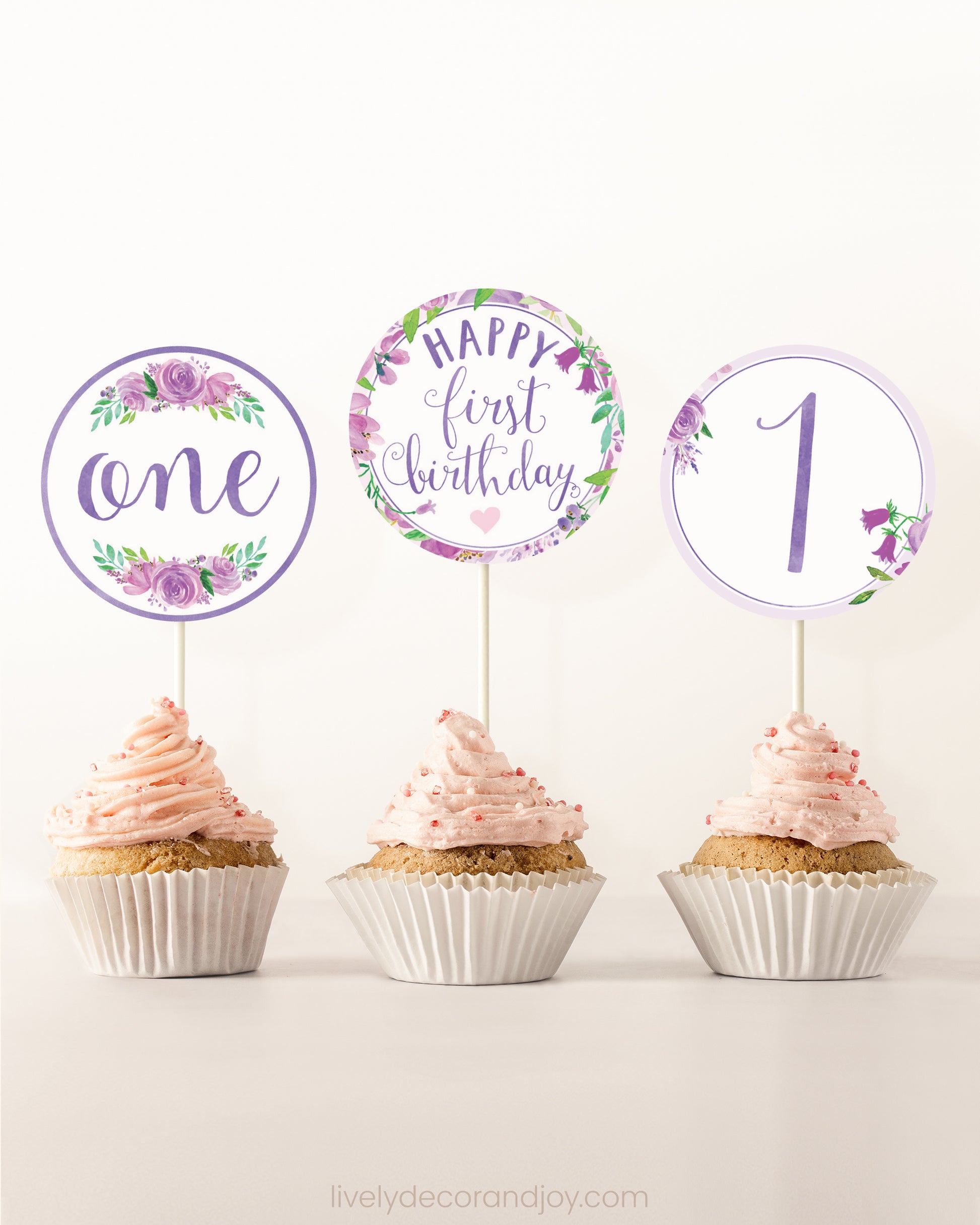 Three cupcakes side by side. Each has a round cupcake topper with purple watercolor flowers and purple and gold letters.
