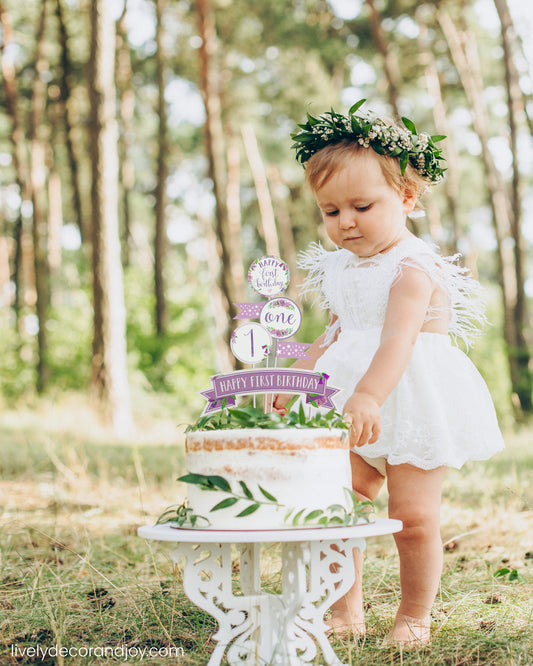 A cute little girl next to her healthy smash cake in a park. It is a rustic sponge cake with a printed cake topper.