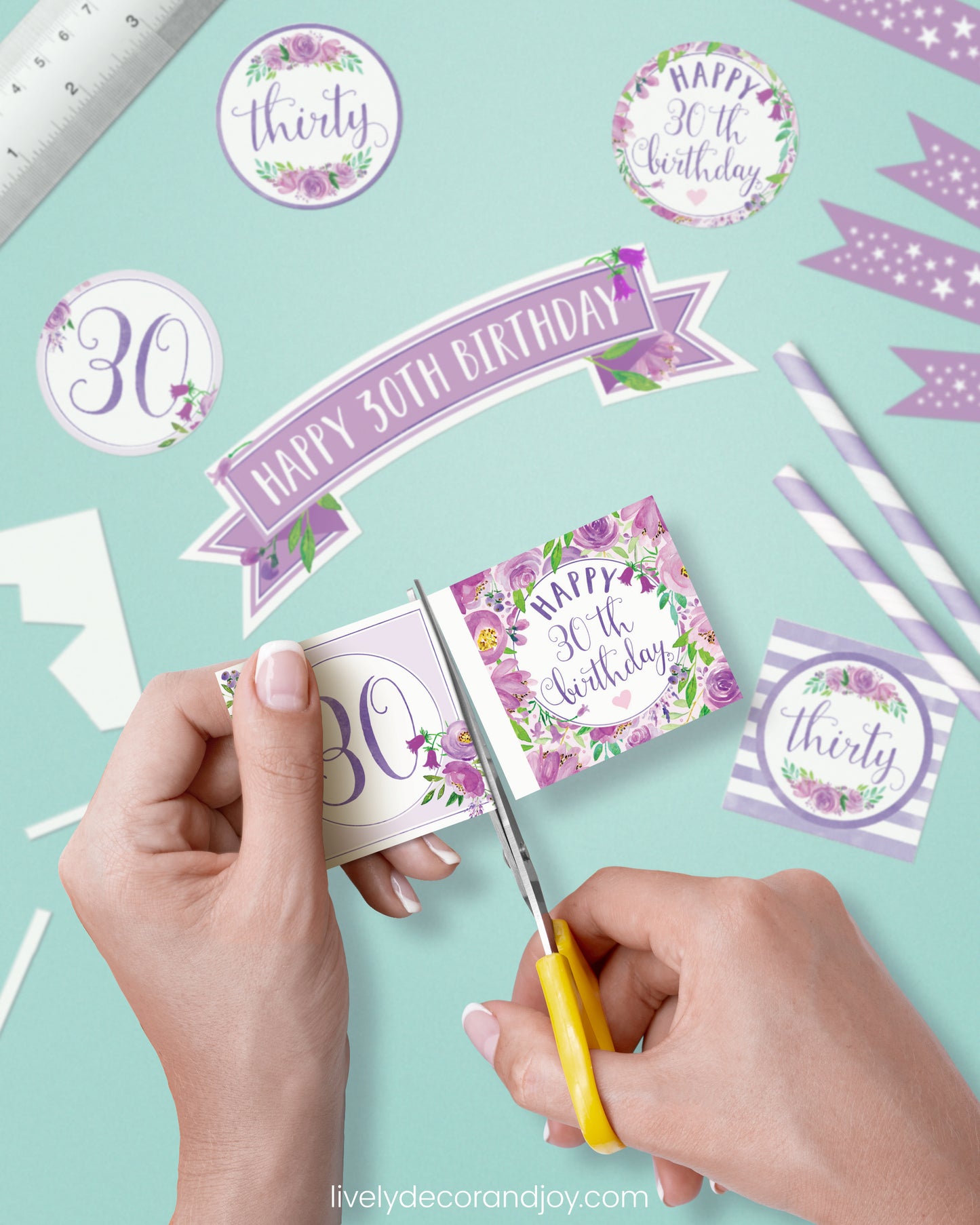 A woman cut a couple of square birthday tags after cutting round party labels, straw flags, and a cake topper.