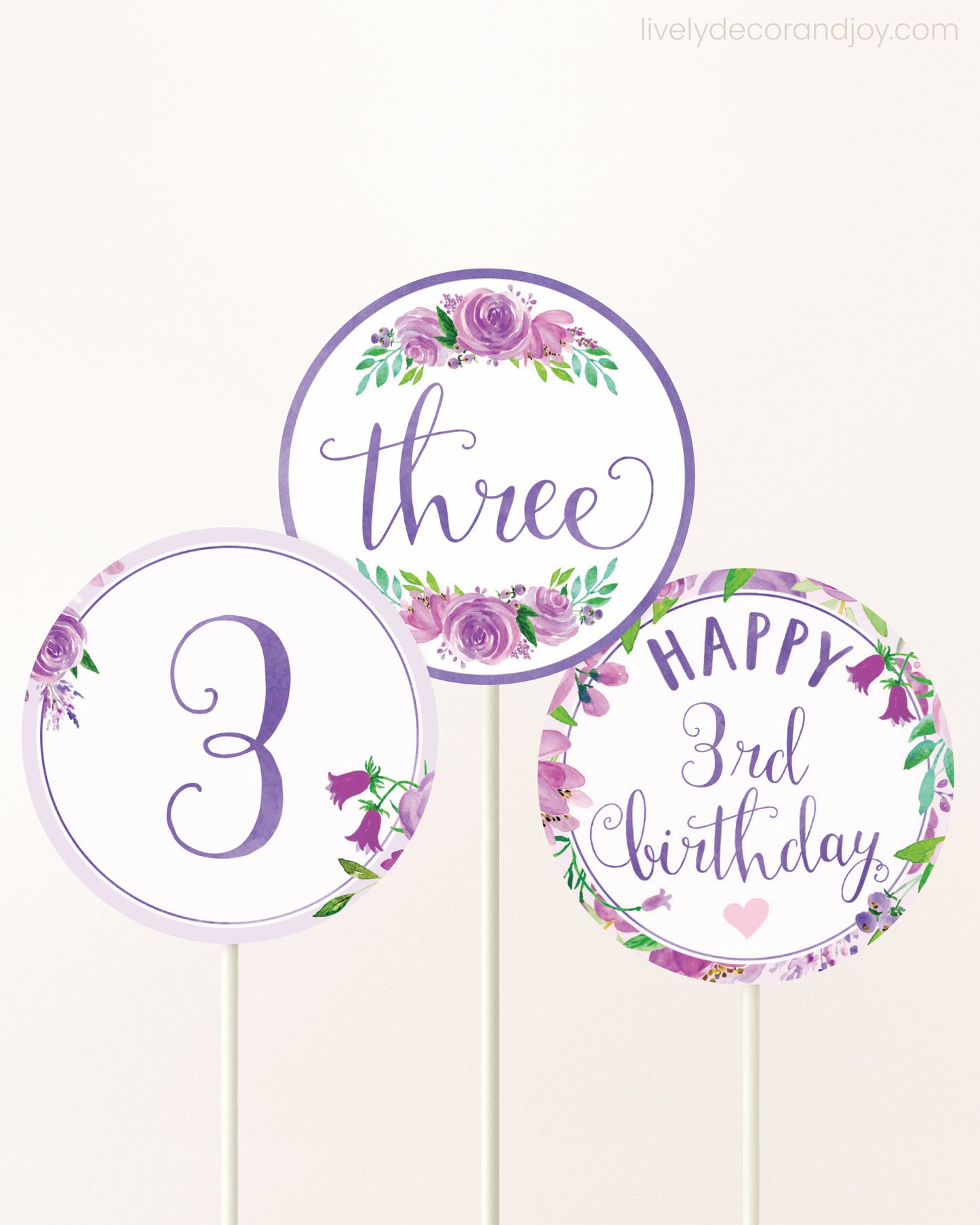 Three DIY toppers attached to lollipop sticks. They show printable cupcake topper designs with purple watercolor flowers.