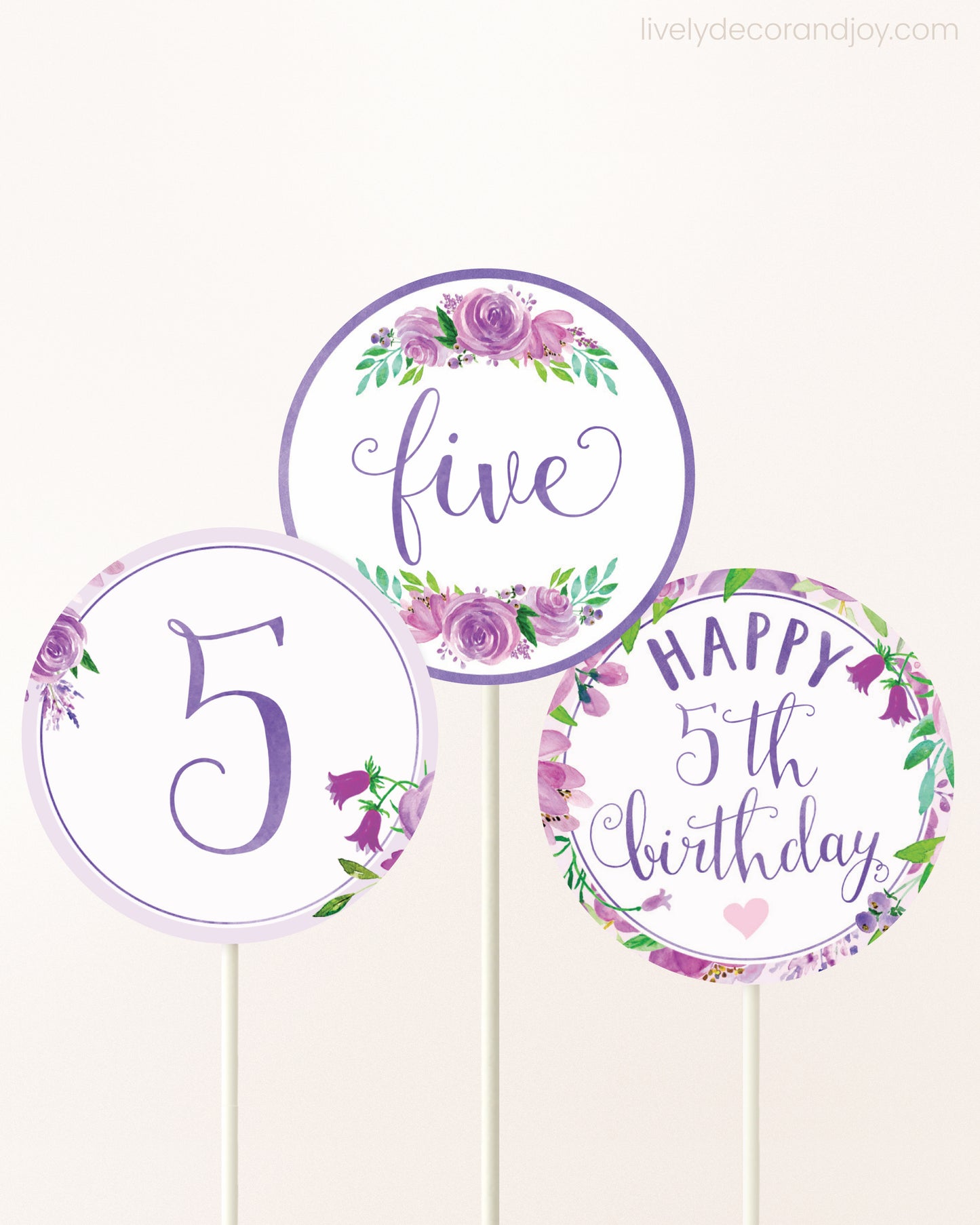 Three DIY toppers attached to lollipop sticks. They show printable cupcake topper designs with purple watercolor flowers.