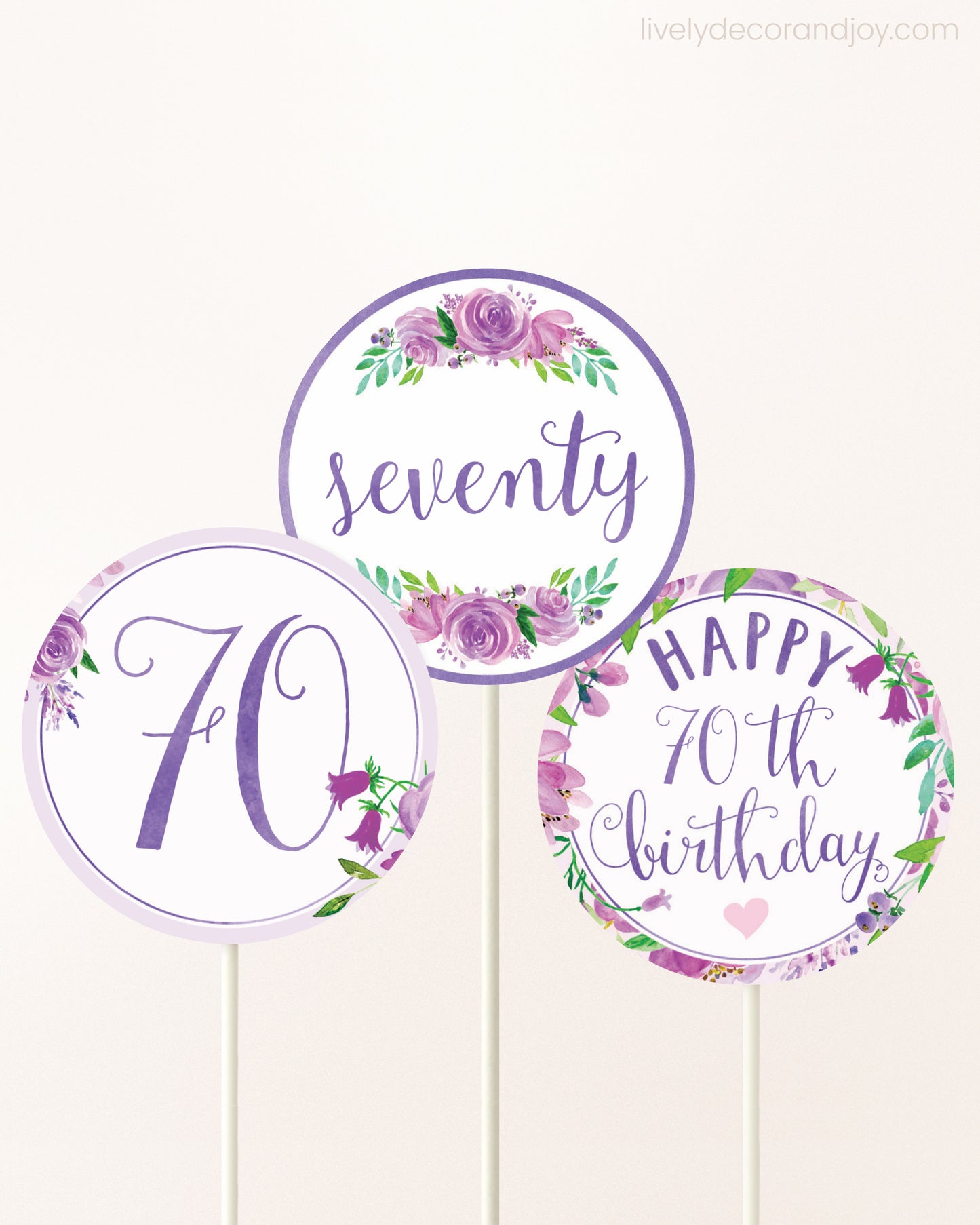Three cupcakes toppers attached to lollipop sticks. They feature purple watercolor floral designs and purple and gold handwritten text.