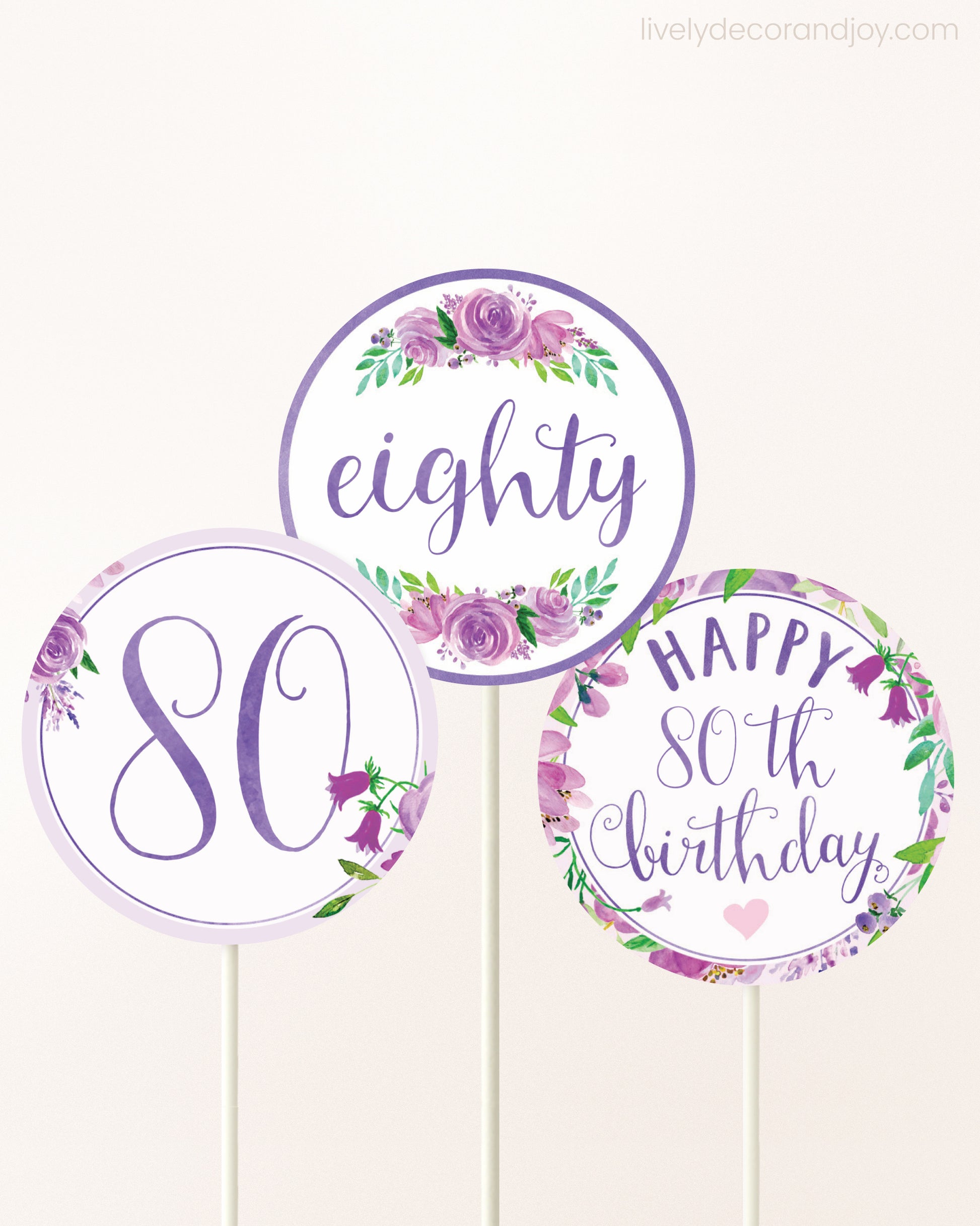 Three DIY toppers attached to lollipop sticks. They show printable cupcake topper designs with purple watercolor flowers.
