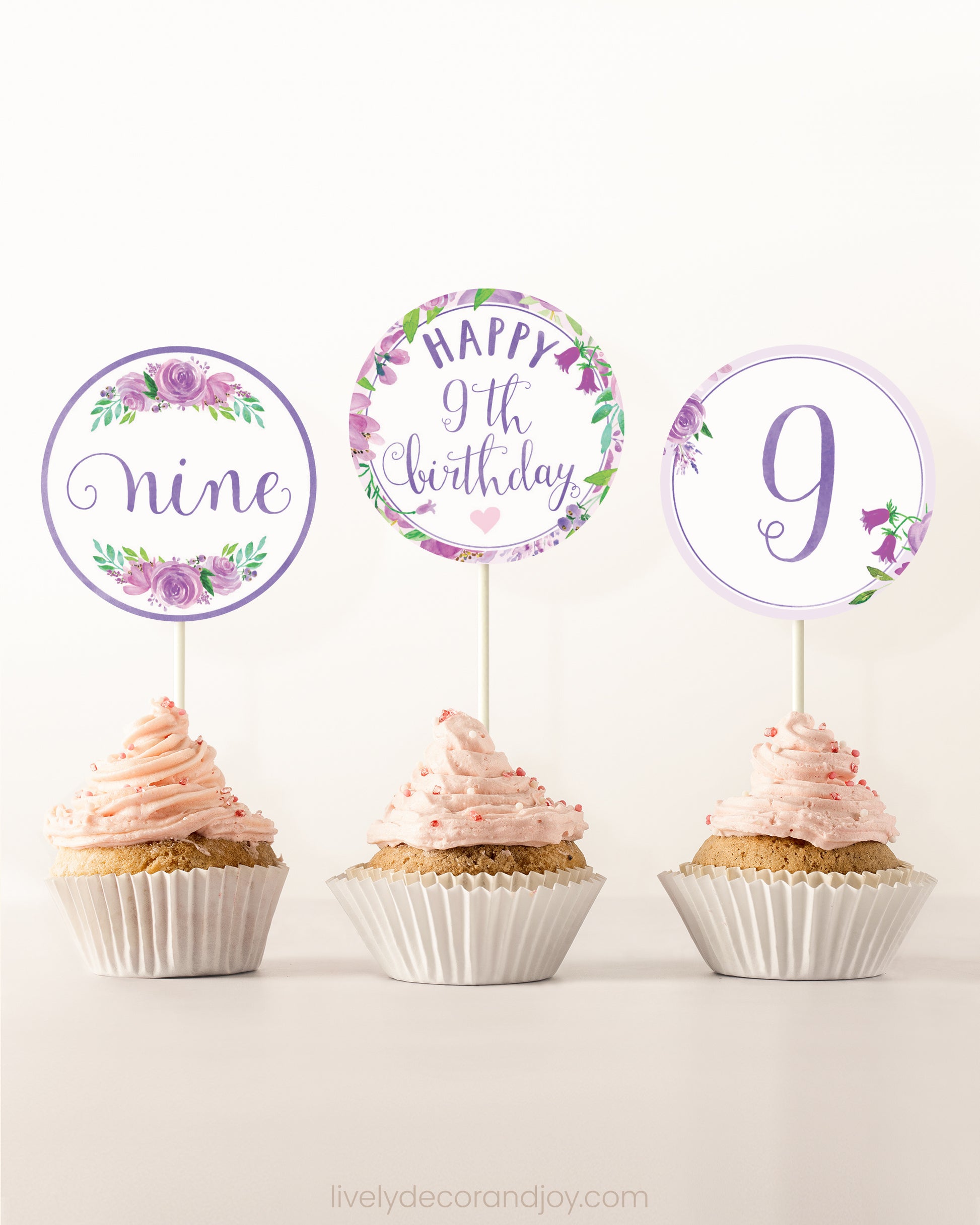 Three cupcakes side by side. Each has a round cupcake topper with purple watercolor flowers and purple and gold letters.