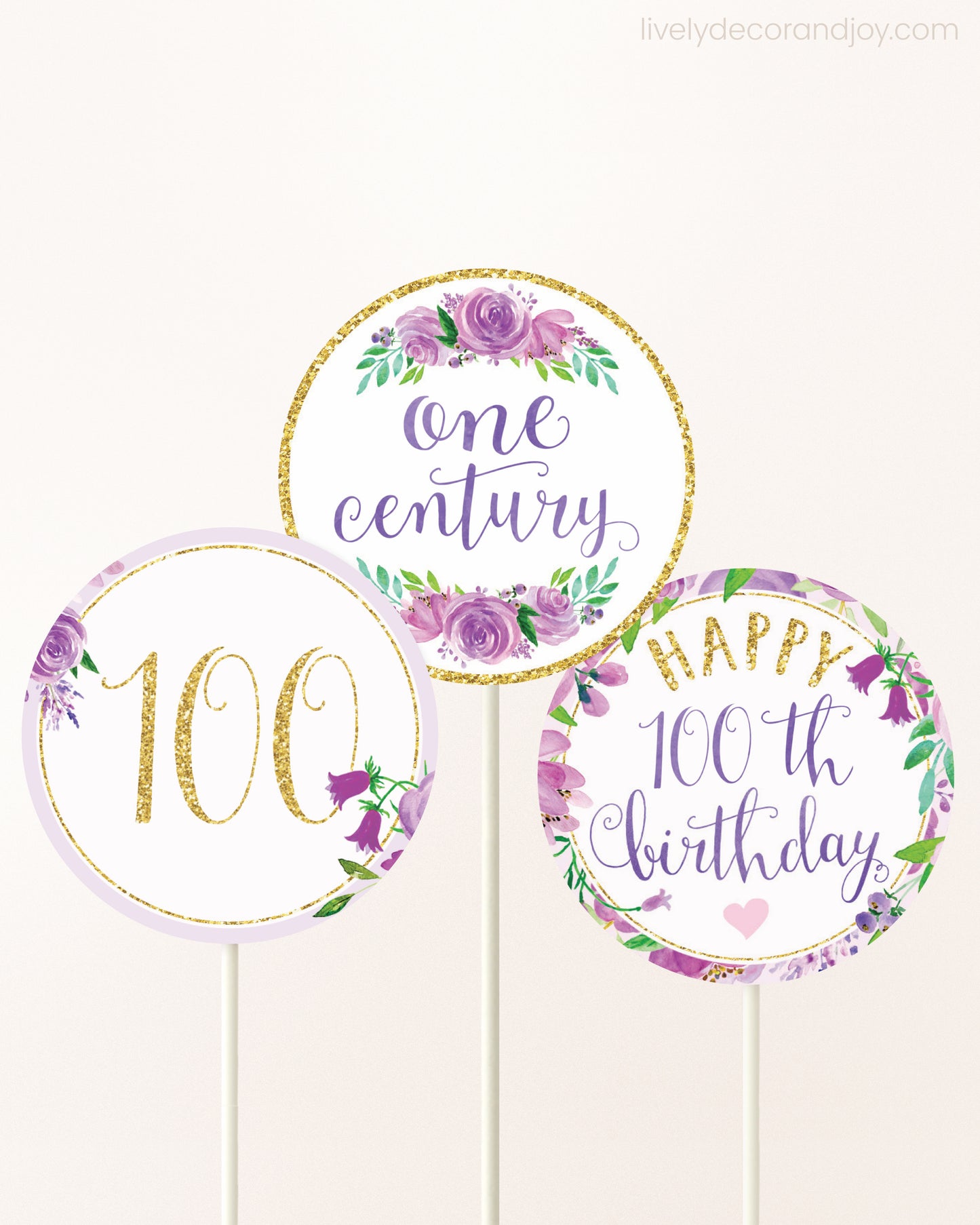 Three cupcakes toppers attached to lollipop sticks. They feature purple watercolor floral designs and purple and gold handwritten text.