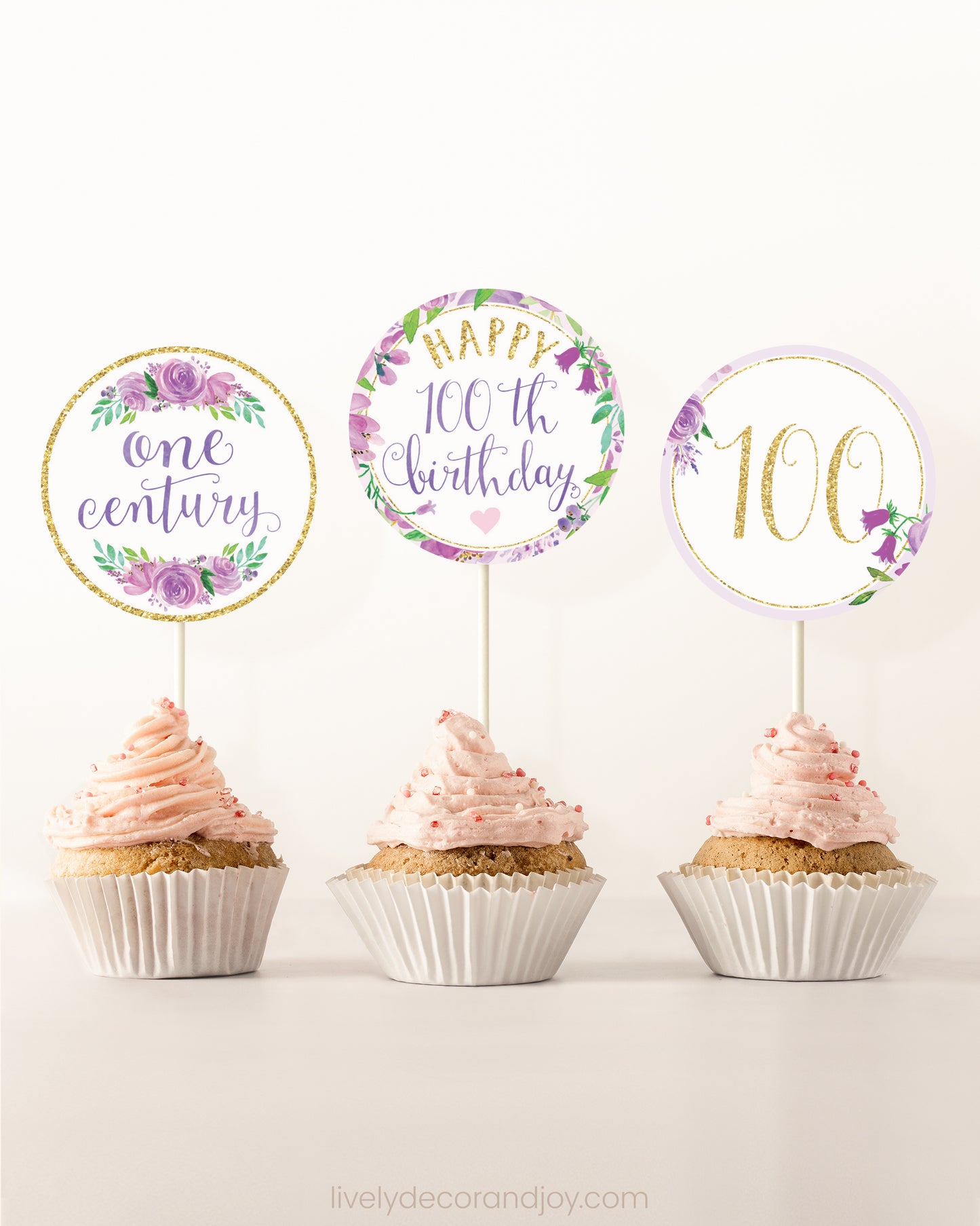 Three cupcakes on a dessert table. Each has a round cupcake topper with purple watercolor floral designs and purple and gold letters.