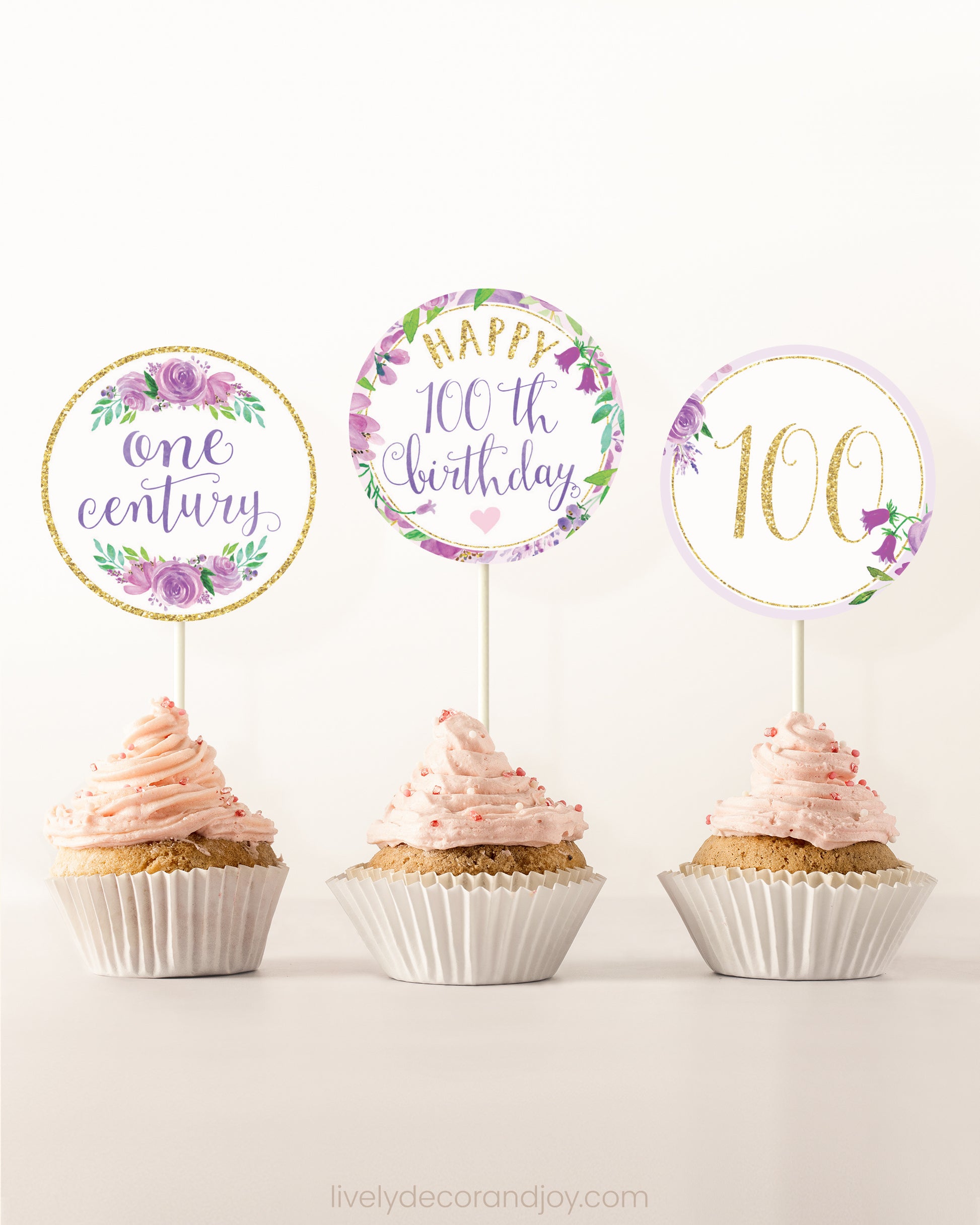 Three cupcakes on a dessert table. Each has a round cupcake topper with purple watercolor floral designs and purple and gold letters.