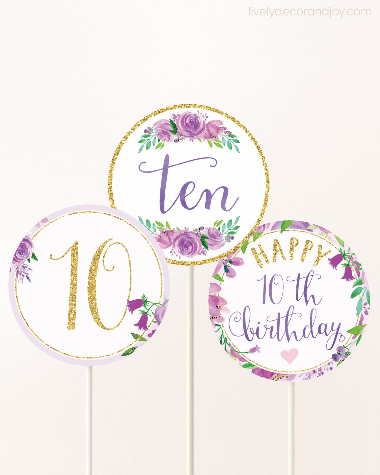 Three cupcakes toppers attached to lollipop sticks. They feature purple watercolor floral designs and purple and gold handwritten text.