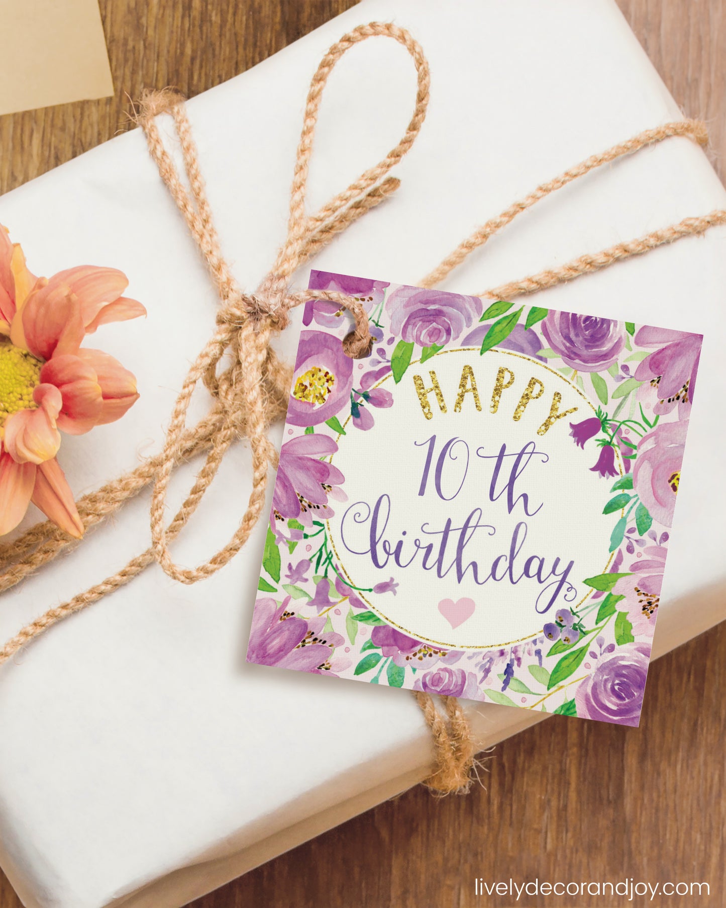 A square gift tag is attached to a birthday gift on a wooden table.